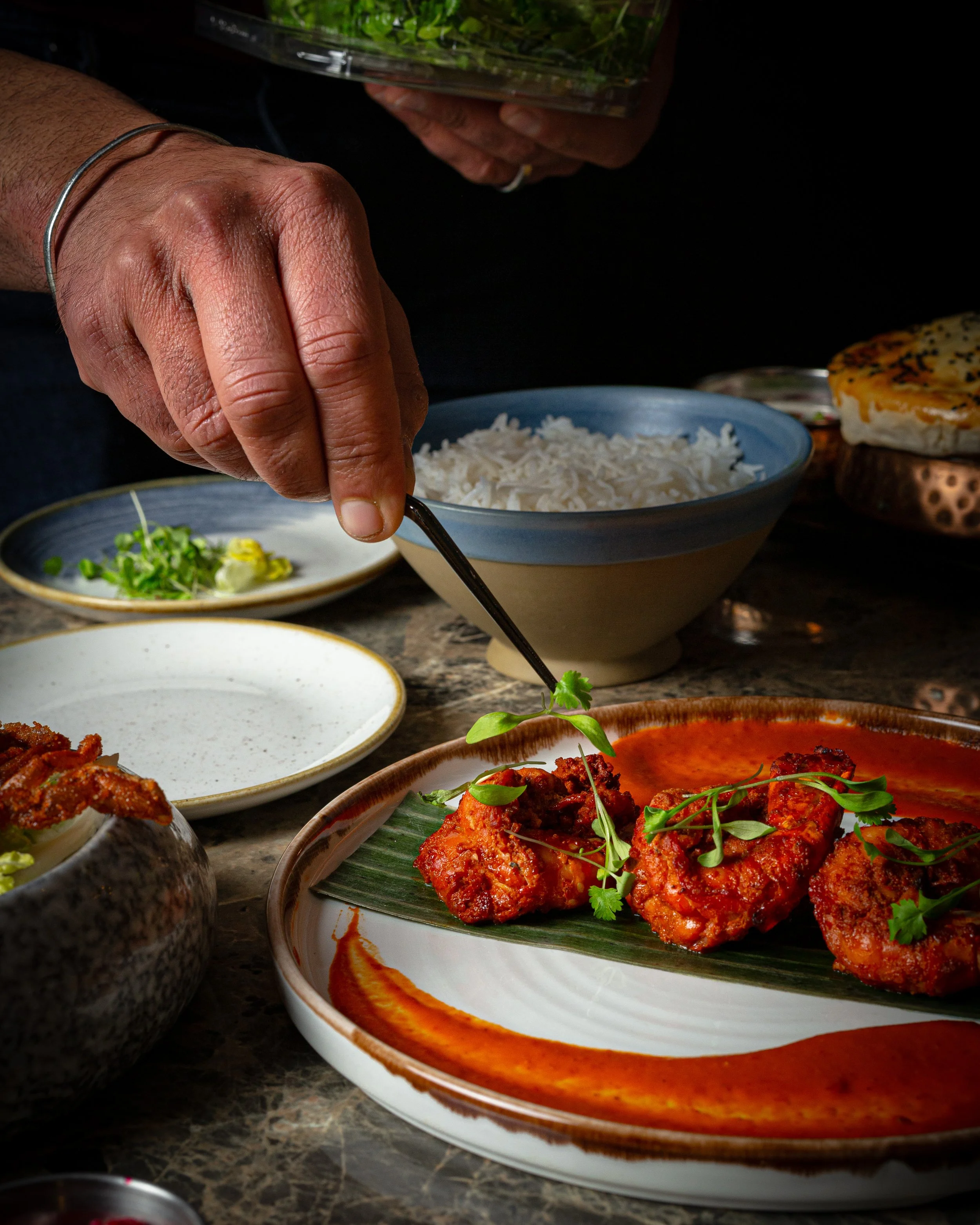 Chef garnishing a chilli-coated dish on banana leaf, with basmati behind
