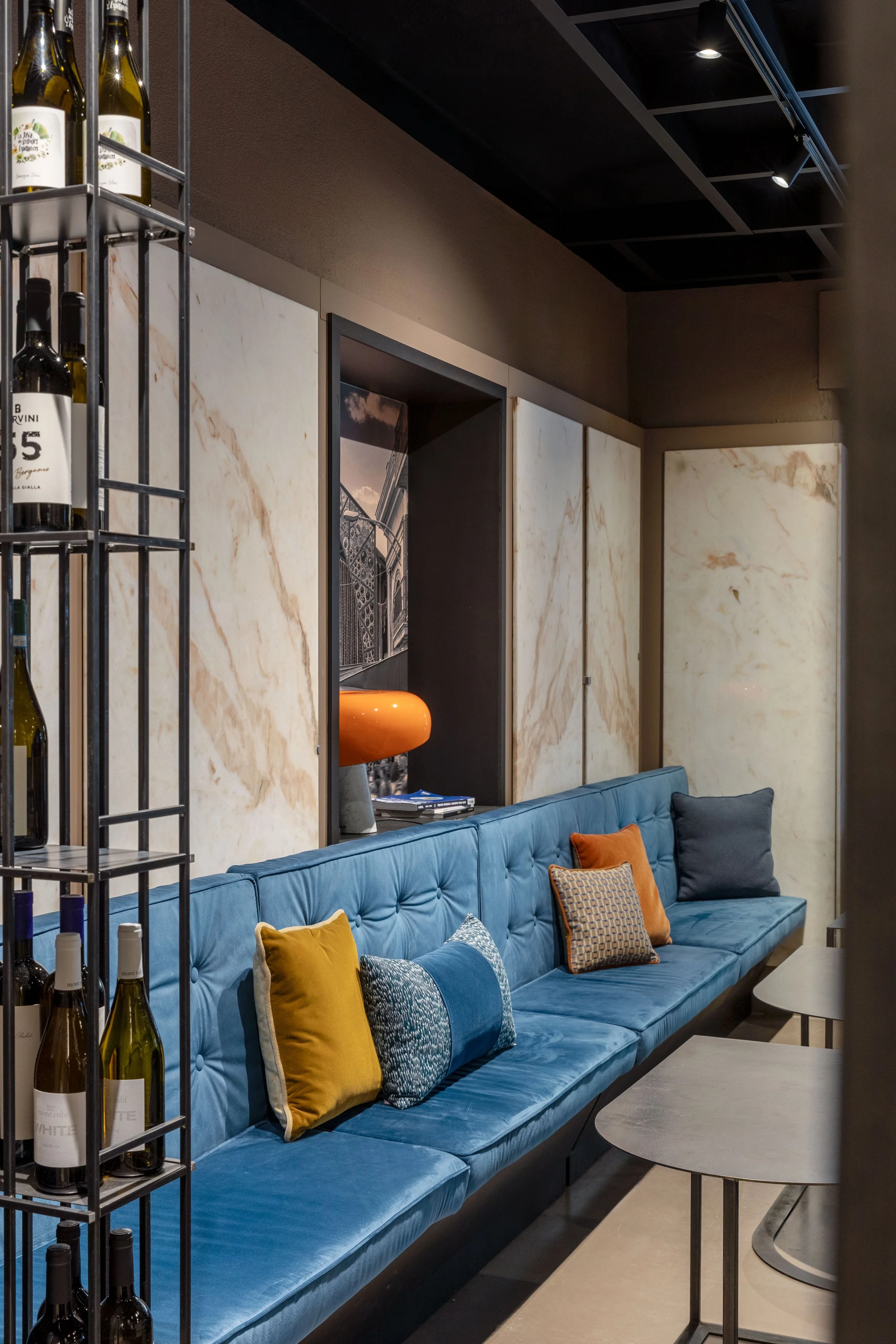 prima sala ristorante con panca progettata ad hoc e rivestita con imbottiti su misura e cuscini decorativi, è stato mantenuto il marmo della vecchia macelleria a parete, i tavoli bassi e il porta vini in ferro sono stati progettati per il ristorante 