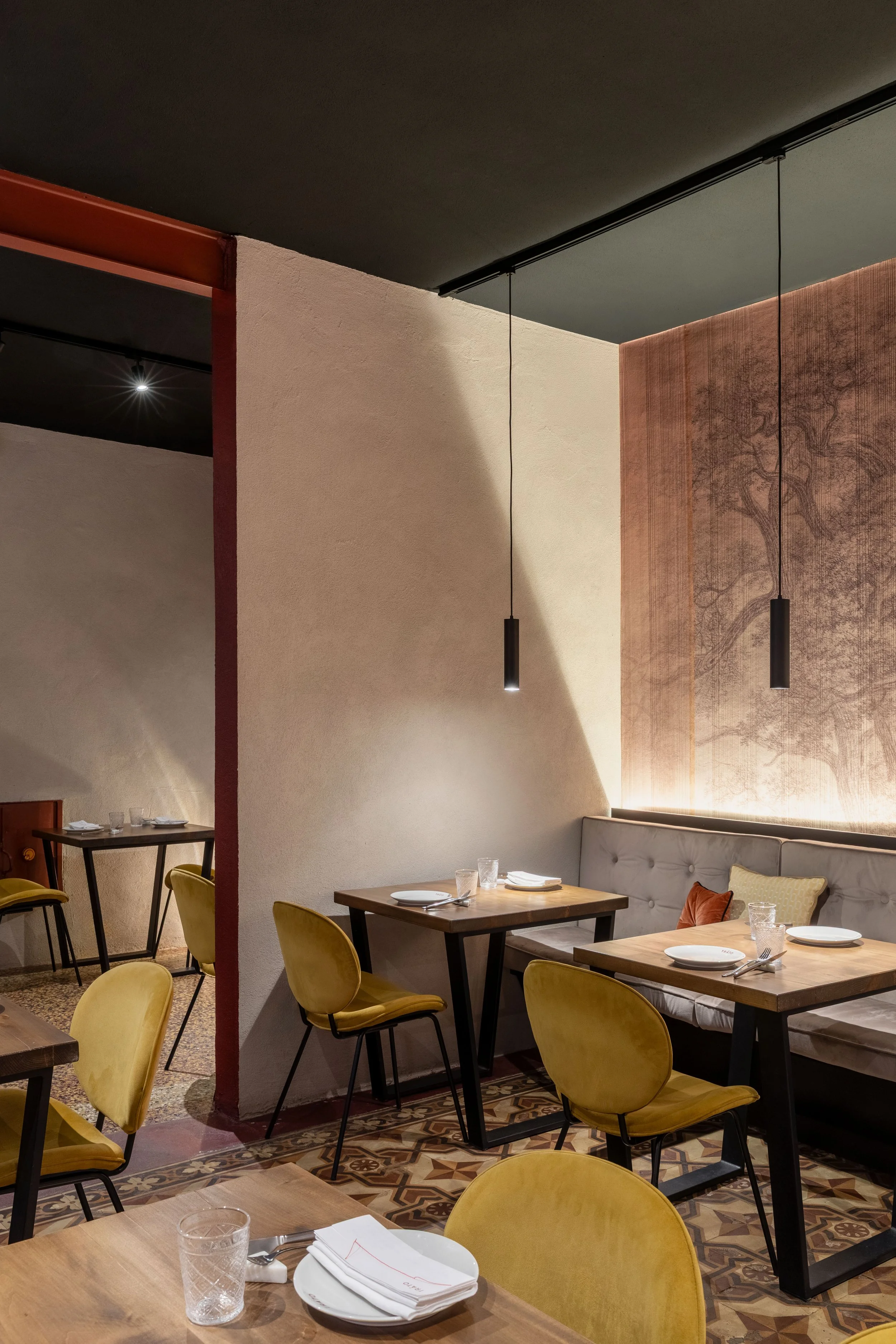 seconda sala ristorante con tavoli in legno su misura, recupero cementine a pavimento, illuminazione ad hoc, carta da parati e putrella con colore dell'insegna della vecchia macelleria