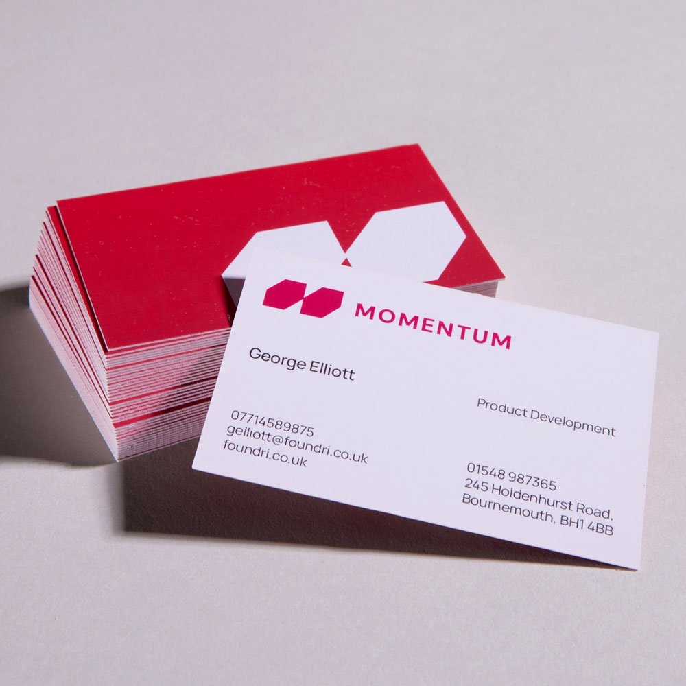 Business cards with the logo 'Momentum' and contact details, one card partially covering a stack of red and white folded cards on a light surface.