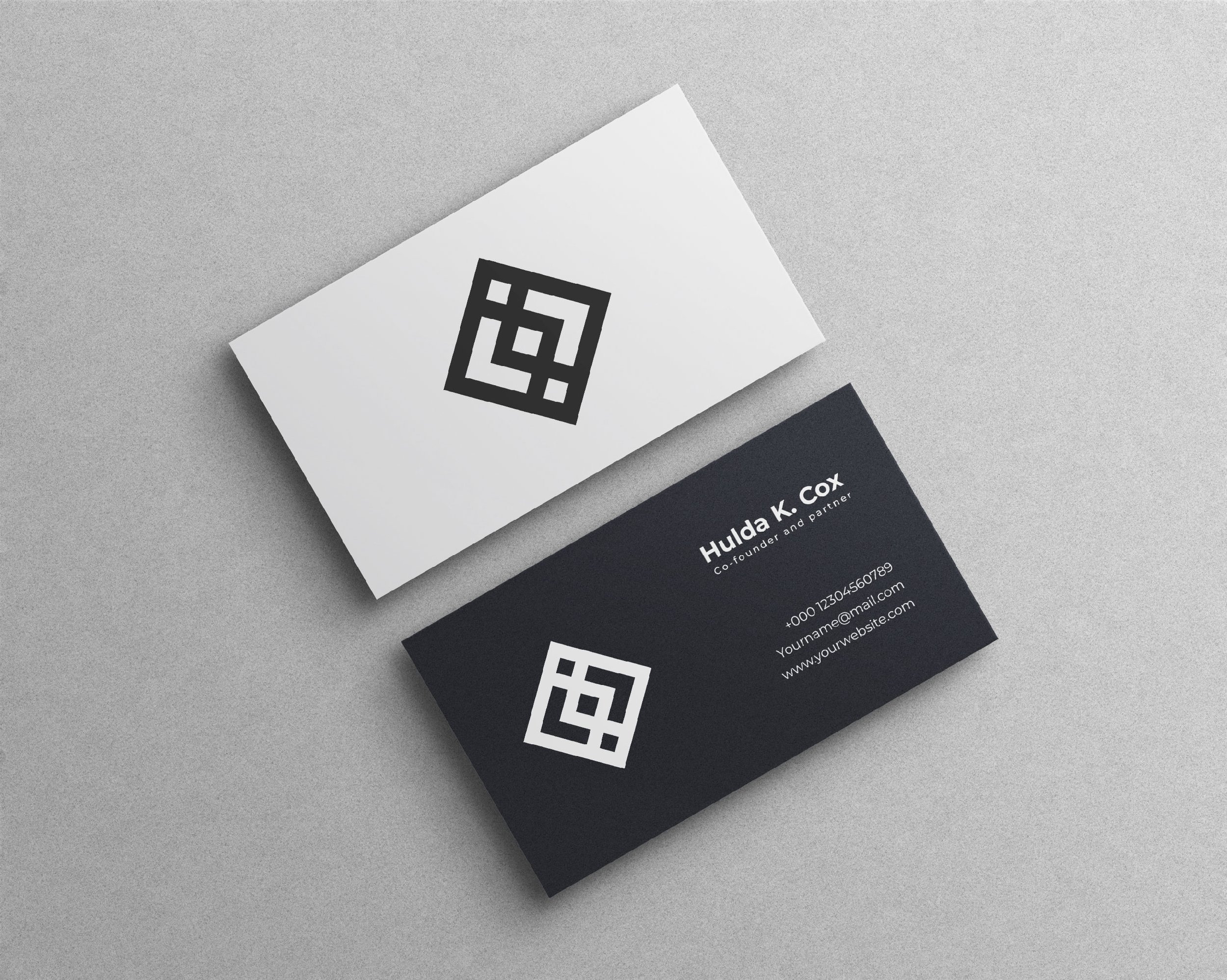 Business cards with black and white designs on a light gray surface, featuring logos and contact details.