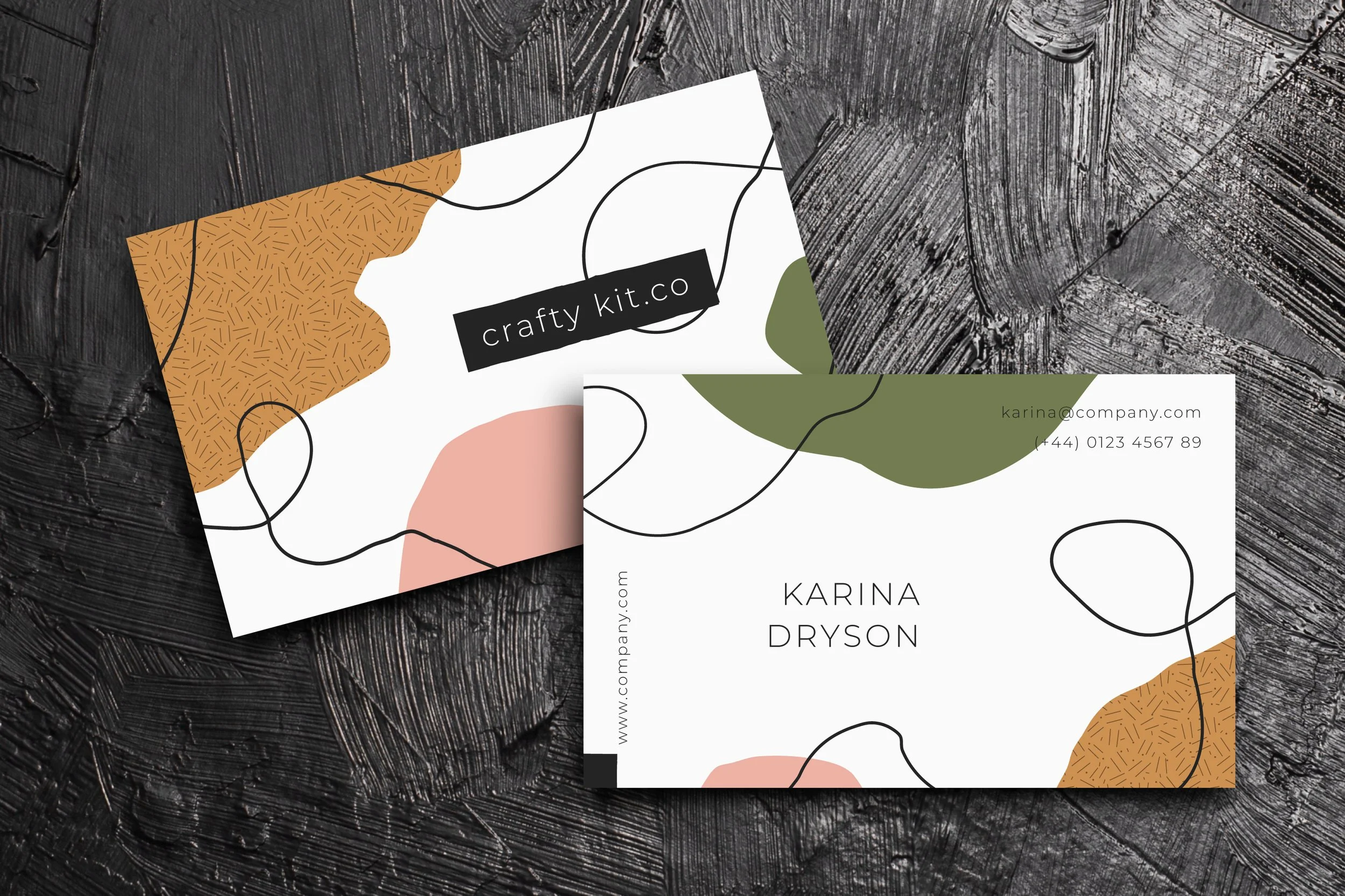 Business cards with abstract designs, one shows the name Karina Dryson and contact information, placed on a dark wooden surface.
