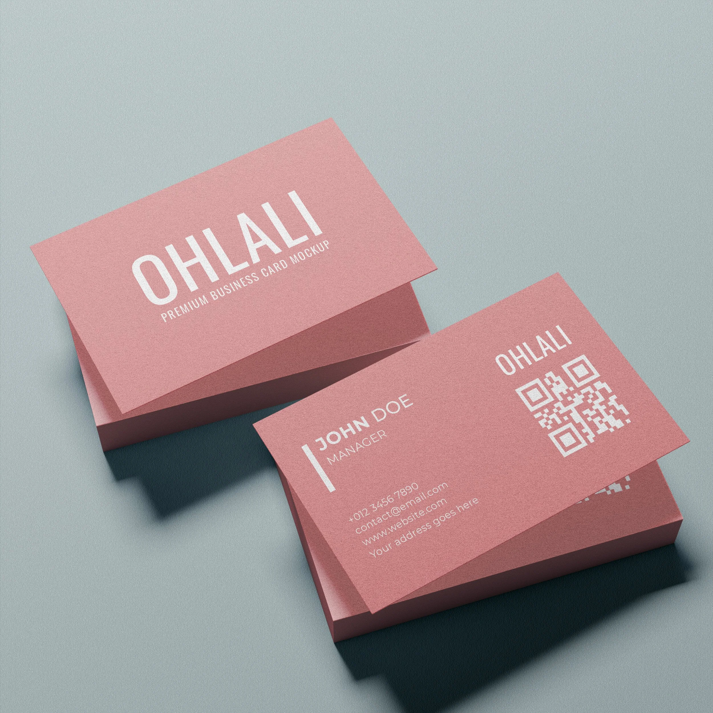 Close-up image of coral pink business cards stacked on a textured light blue surface, with the front card displaying white text 'OHLAI' and a QR code.