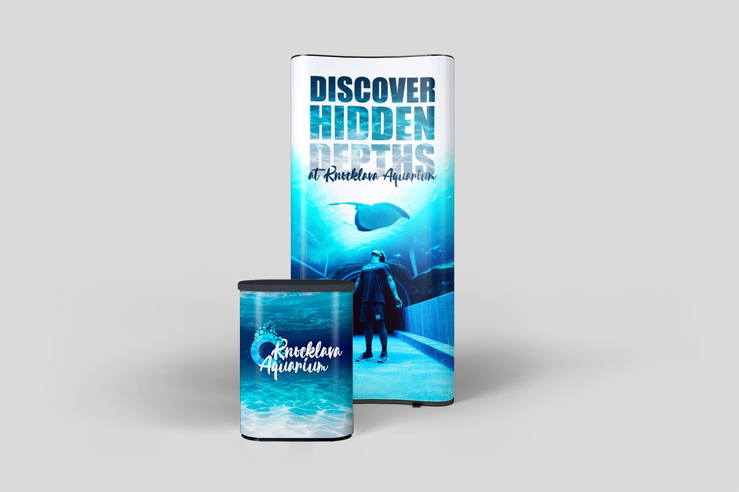 Promotional display for Knicklava Aquarium featuring an underwater scene with a diver and stingray, and a large vertical banner with text about discovering hidden depths at Knicklava Aquarium.