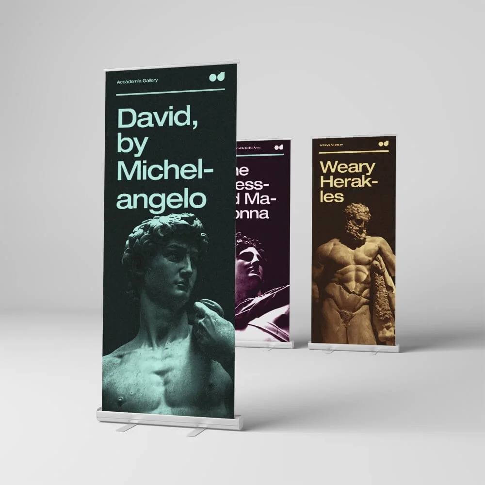 Three vertical banners displayed on the floor, advertising art exhibitions at an academic gallery. The first banner features a classical sculpture of David by Michelangelo, with text stating "David, by Michelangelo." The second banner, partly visible, shows a face with sunglasses and a person in a hat, with text referencing Madonna. The third banner displays a statue of a muscular man with text reading "Weary Herakles." Each banner has a different background color.