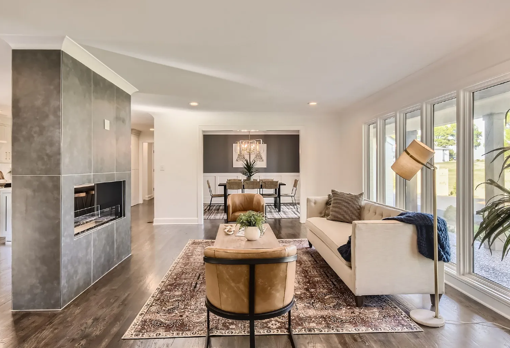 Living room with beige sofa, brown armchair, floor lamp, large windows, and modern decor, adjacent to dining area with table and chairs.