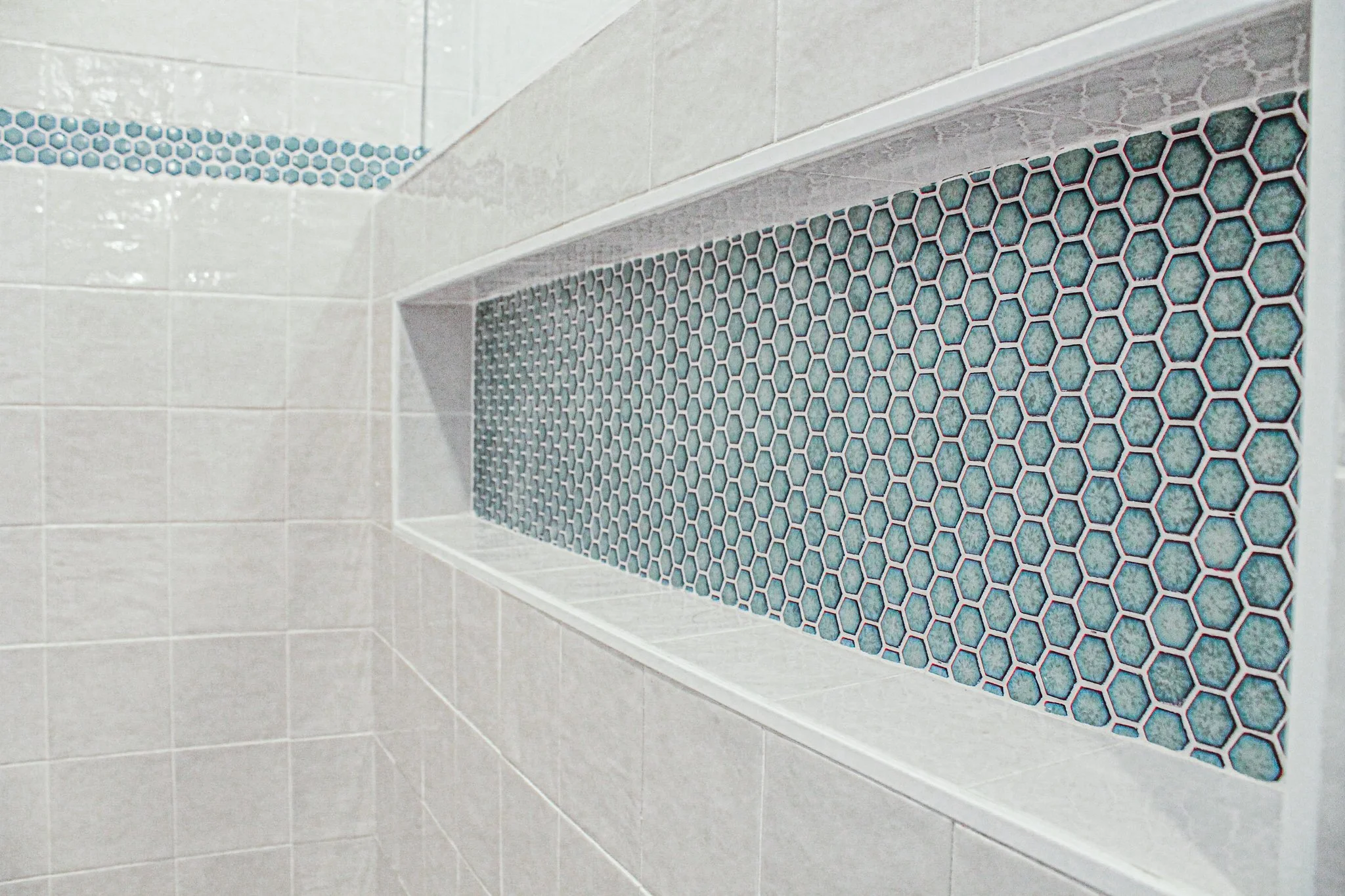 Bathroom shower wall with white tiles and an inset shelf featuring blue hexagonal mosaic tiles.