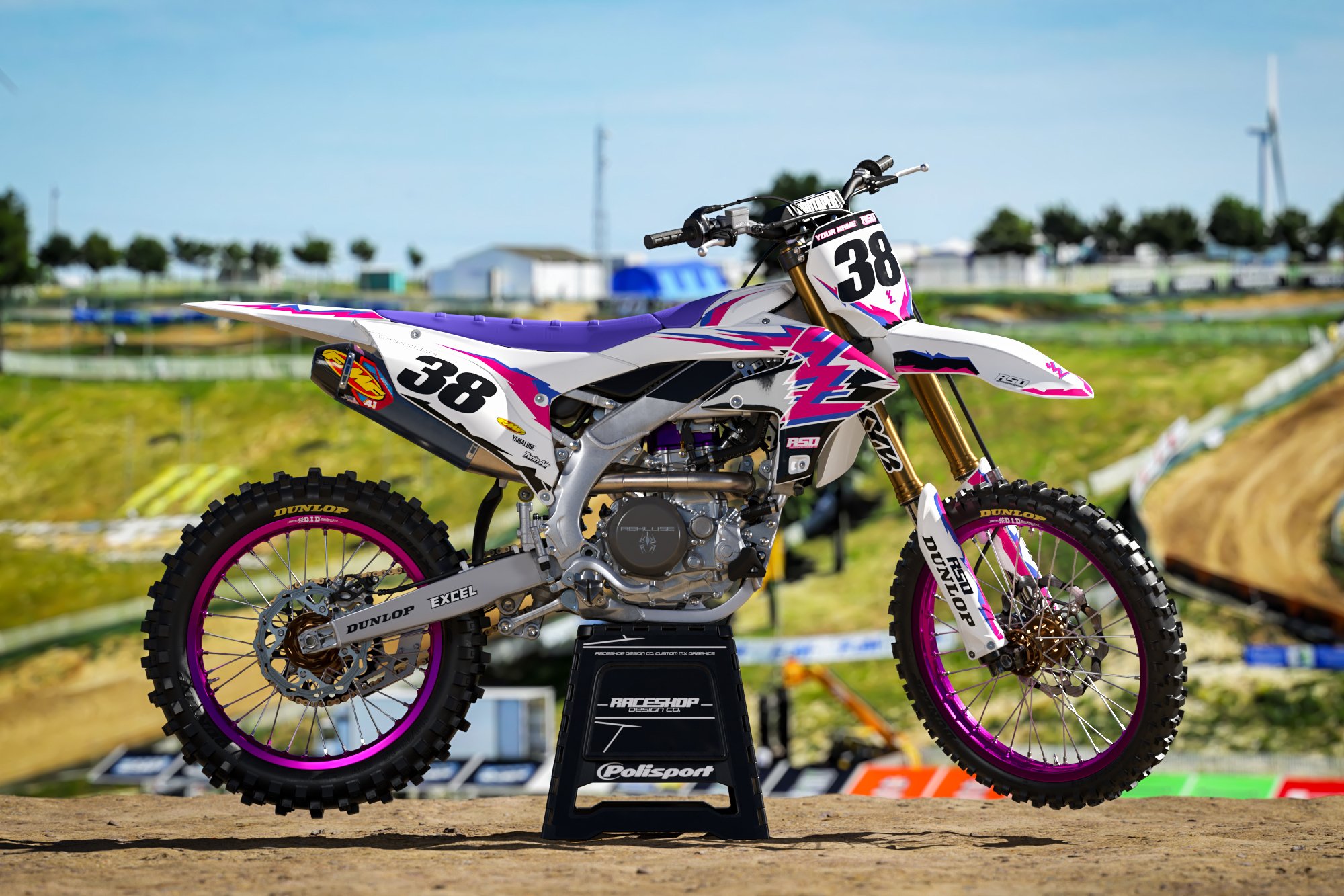 Custom motocross dirt bike with number 38, pink and purple graphics, on a stand in an outdoor track setting with blurred background.