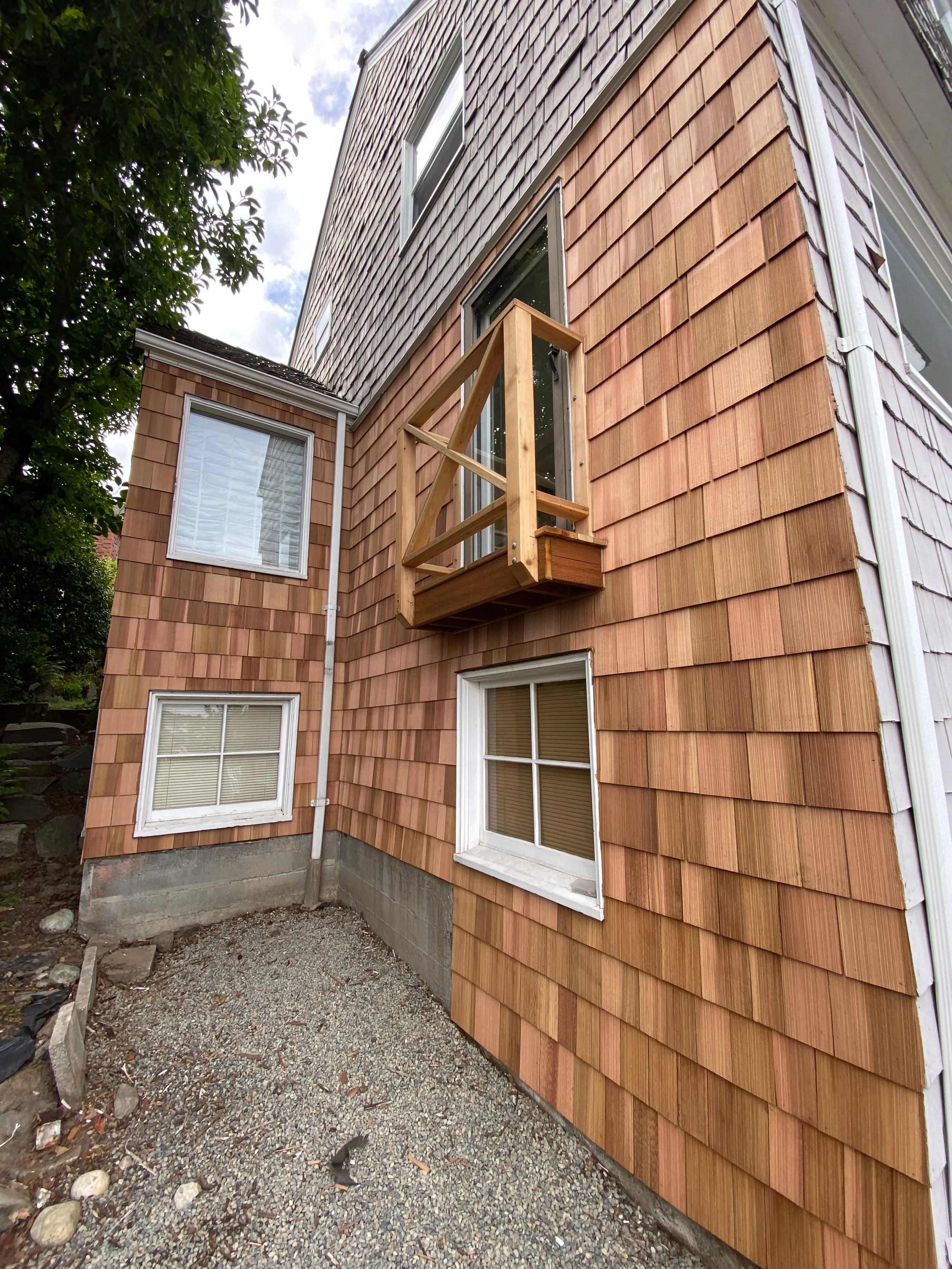A house with wooden siding, two windows, and a small wooden balcony under construction on the second floor.