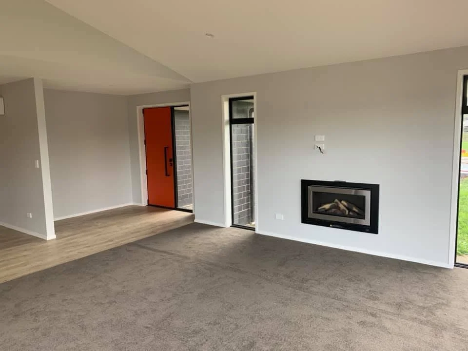 Empty living room with gray walls, brown carpet, a built-in fireplace, and large windows near the door with a brick exterior.