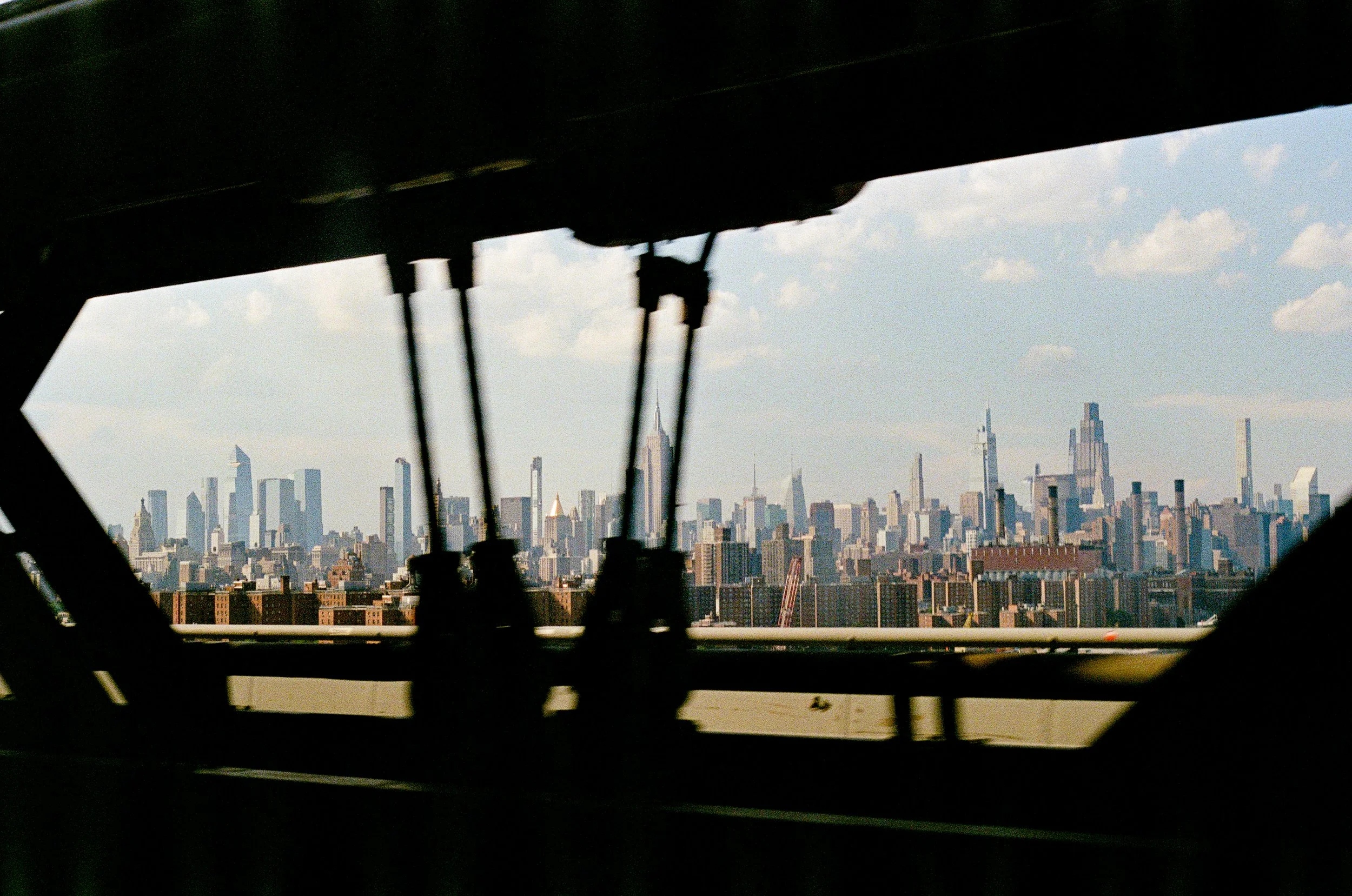 View of the New York City skyline through a gap in a dark structure, with the Empire State Building visible in the distance.