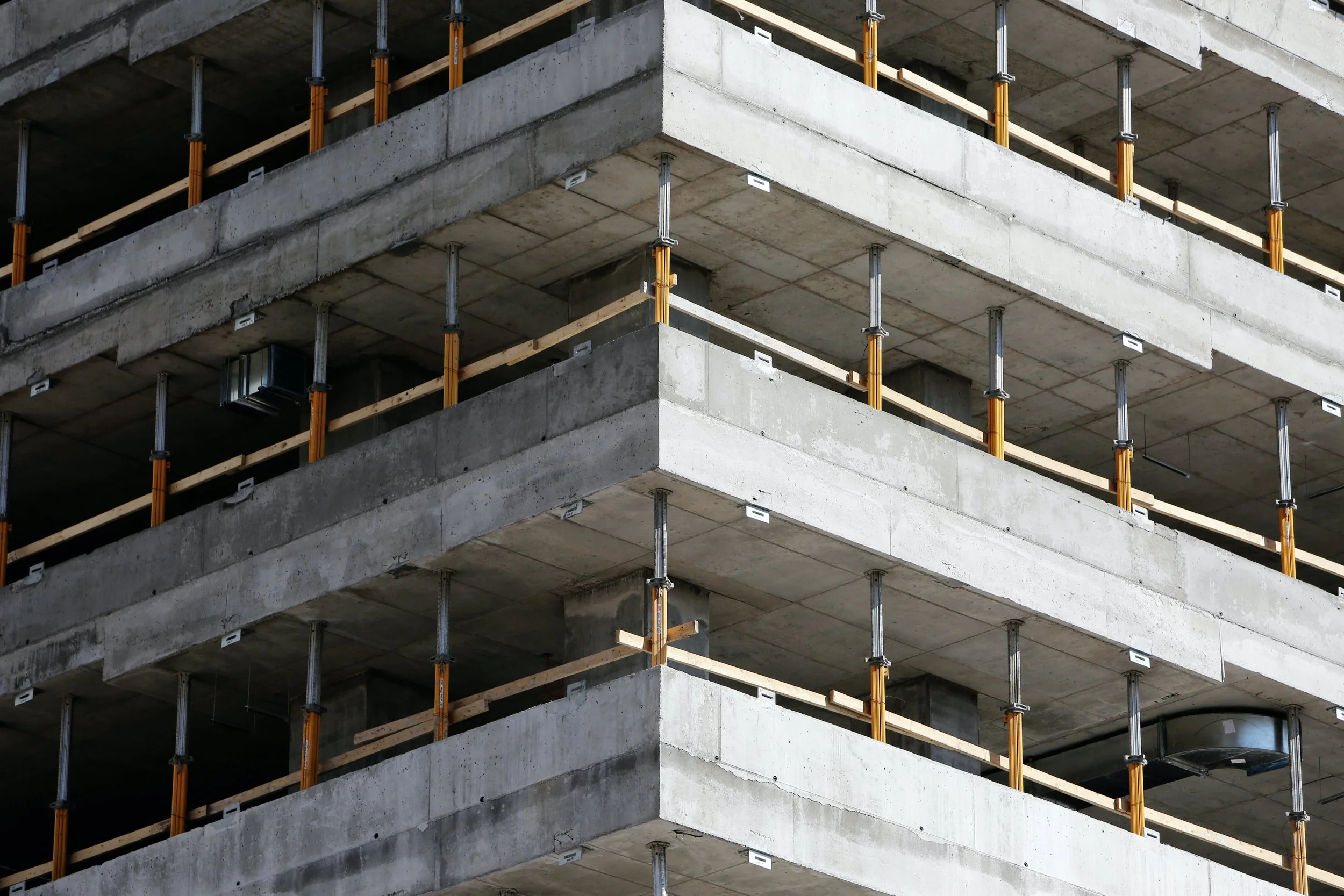 Close-up of a multi-story building under construction with concrete floors, metal support poles, and safety barriers.