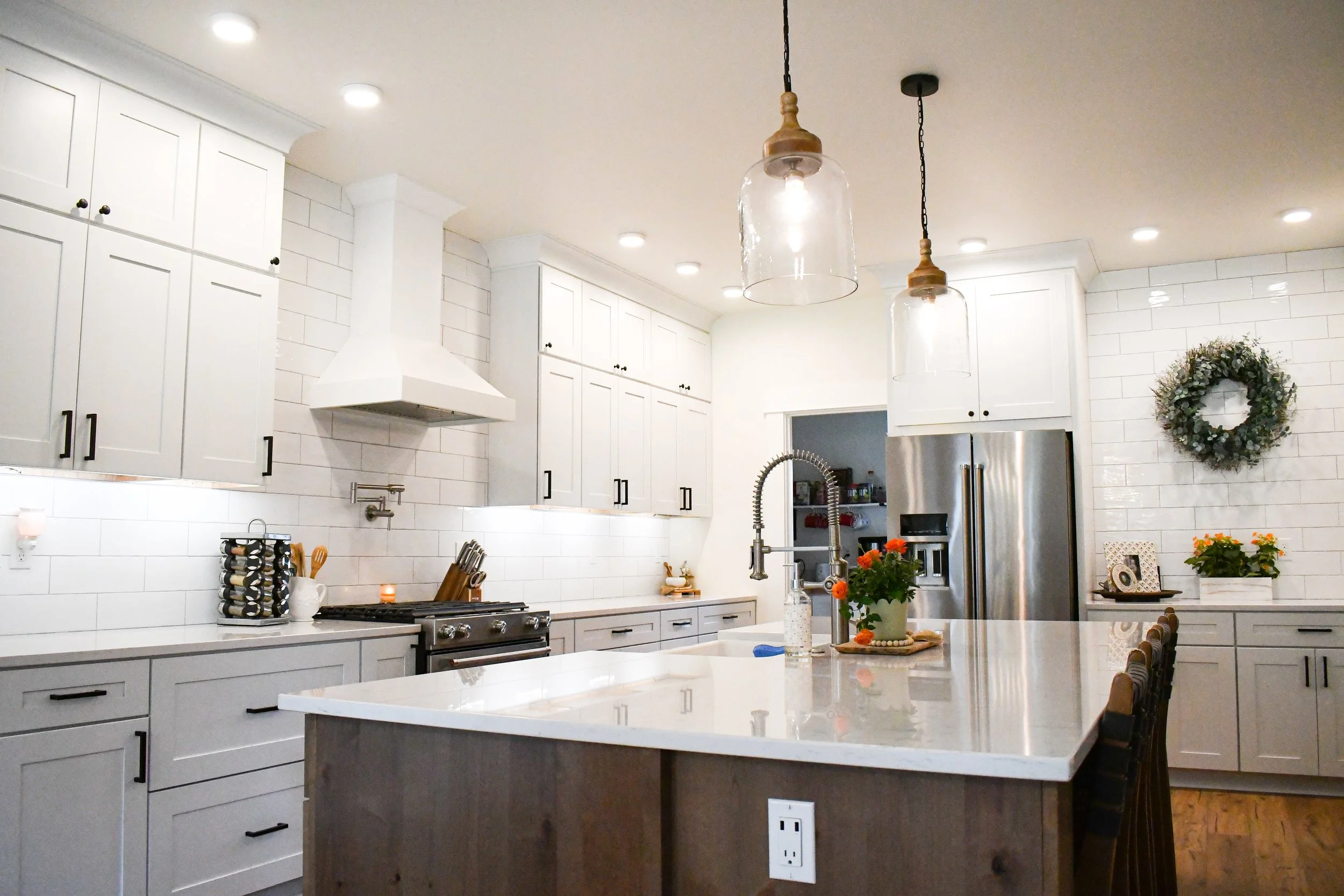 Modern kitchen with white cabinets, a large island with a white countertop, stainless steel appliances, and decorative plants and wreaths.