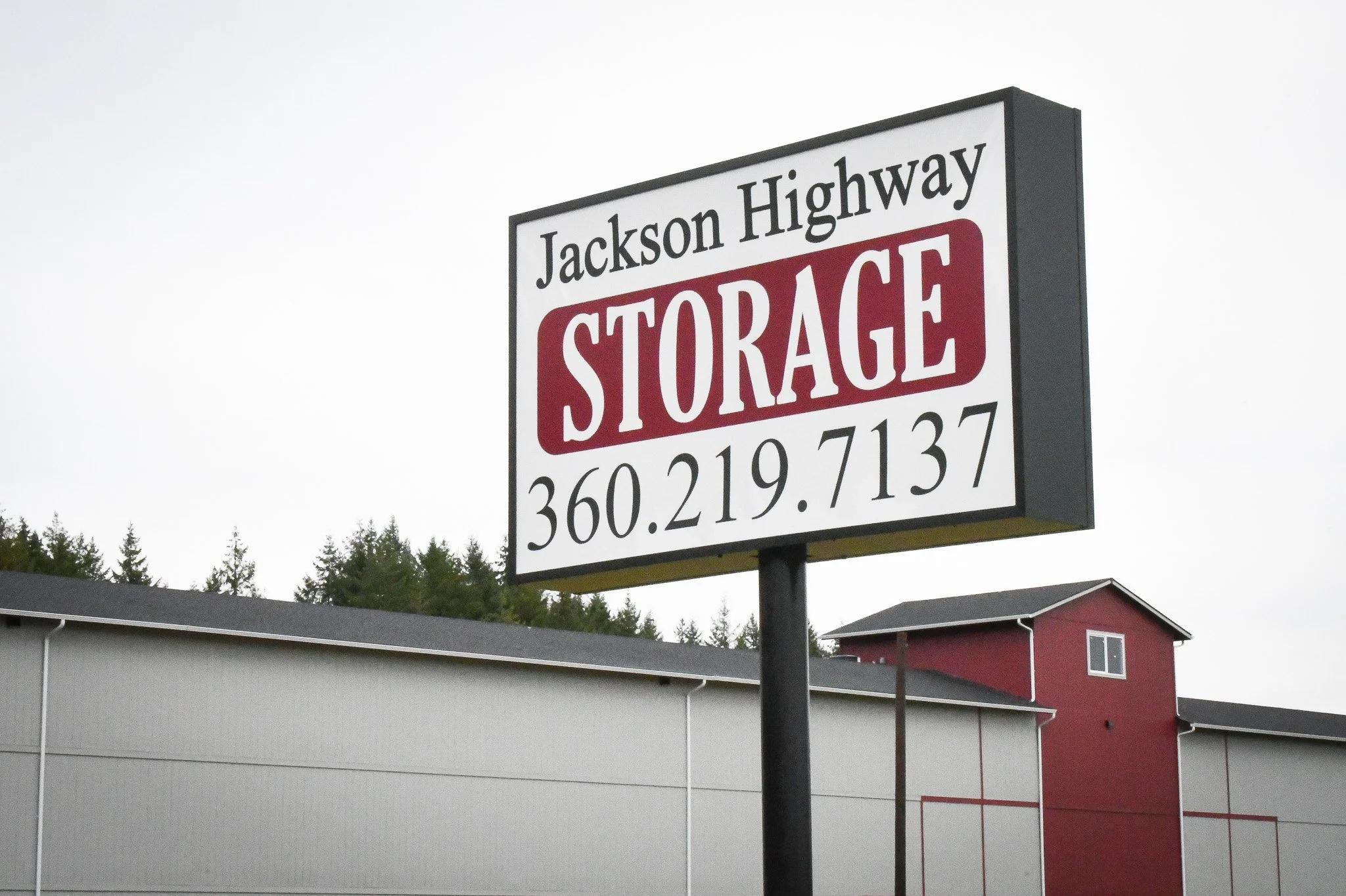 Sign for Jackson Highway Storage with a phone number, against a background of trees and a building.