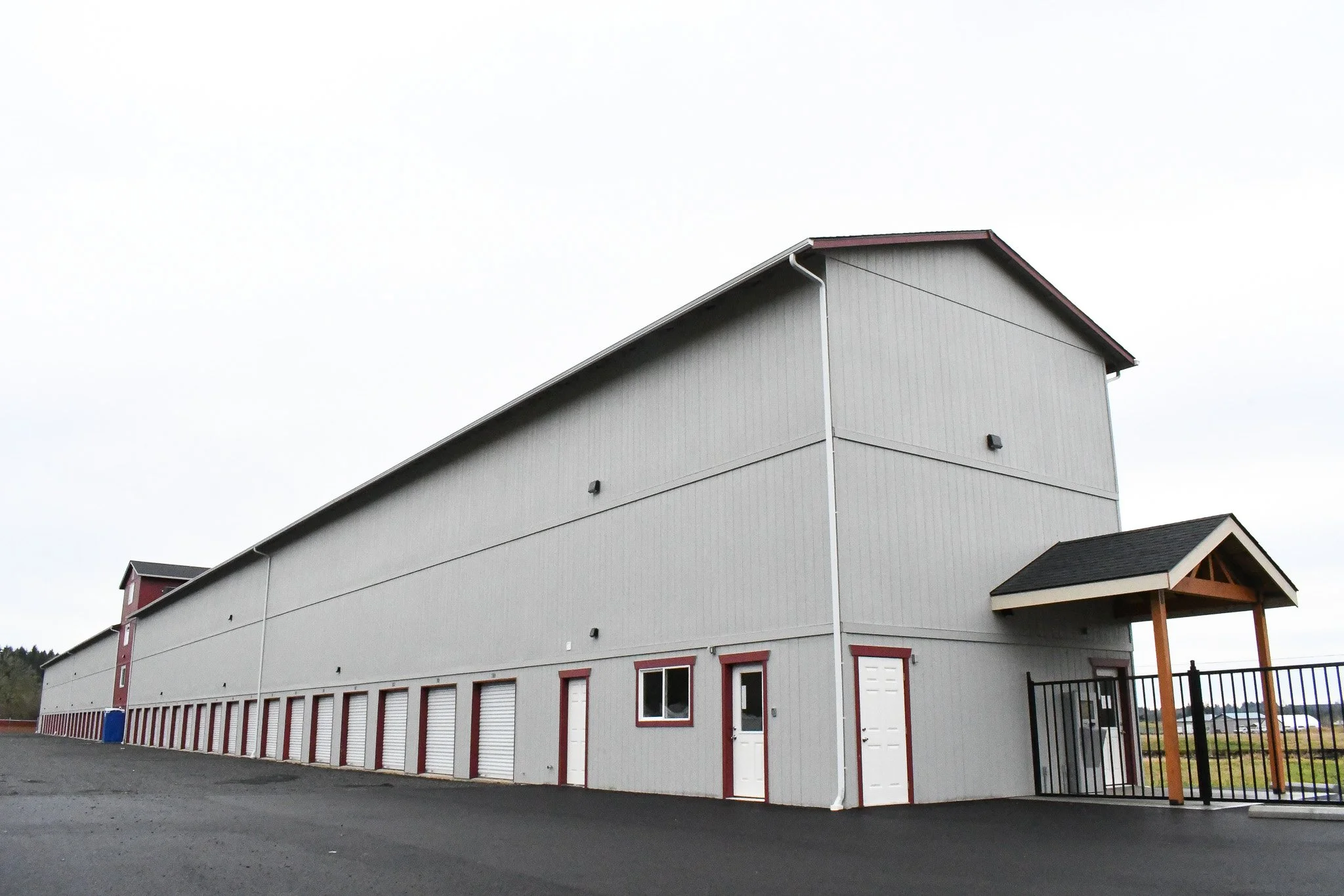 Side view of a large, gray, multi-story storage building with white doors and windows, and a small covered entrance with wooden posts.