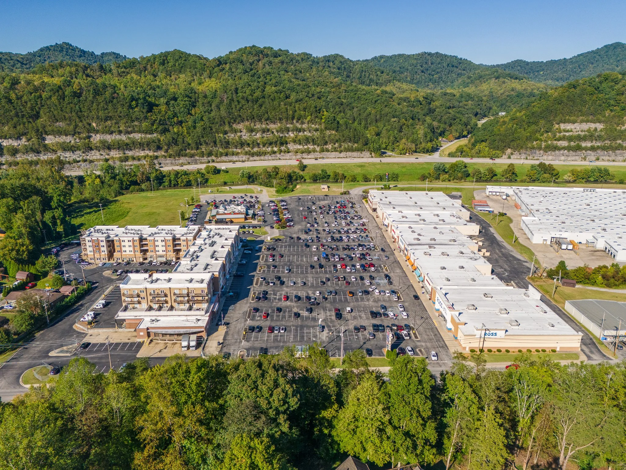 An aerial view of a residential construction site with multiple buildings in various stages of completion, surrounded by open fields and nearby neighborhoods