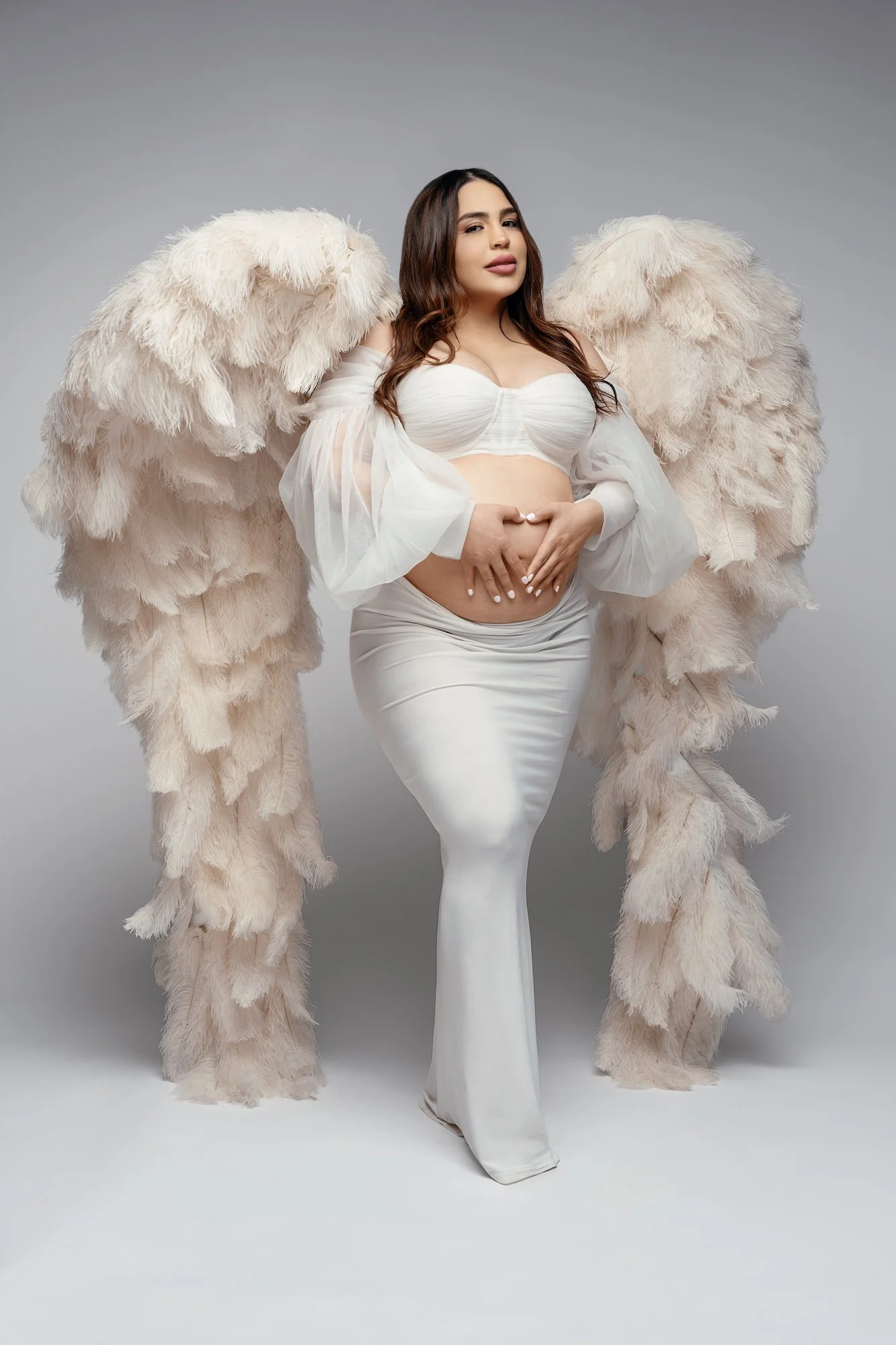 Luxury maternity photoshoot: pregnant woman in a white gown with angel wings