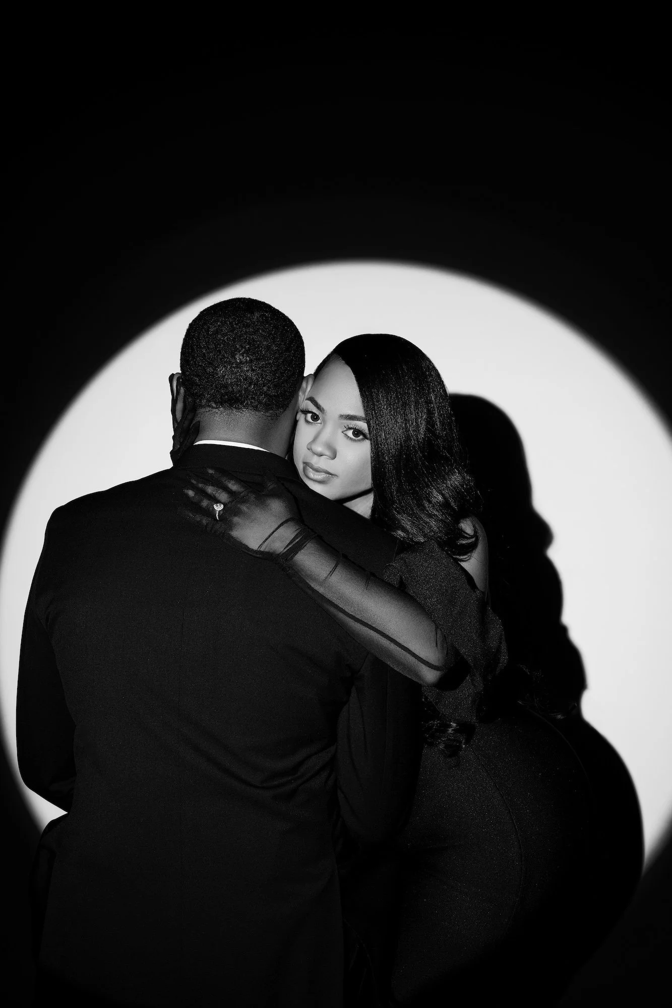 Black and white dramatic spotlight engagement portrait, couple embracing in circle of light, moody studio photography at Filaneyka Chicago