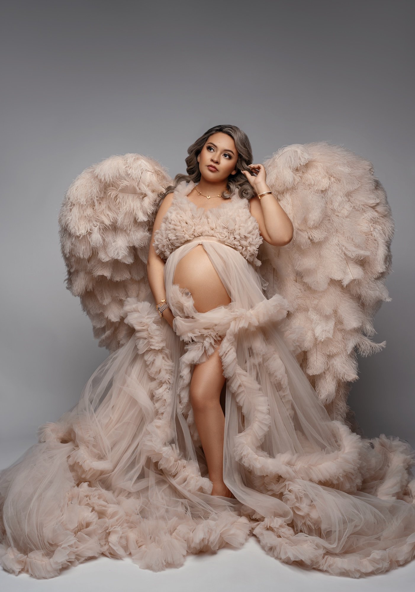 Fine-art maternity portrait: pregnant woman in a beige gown with angel wings