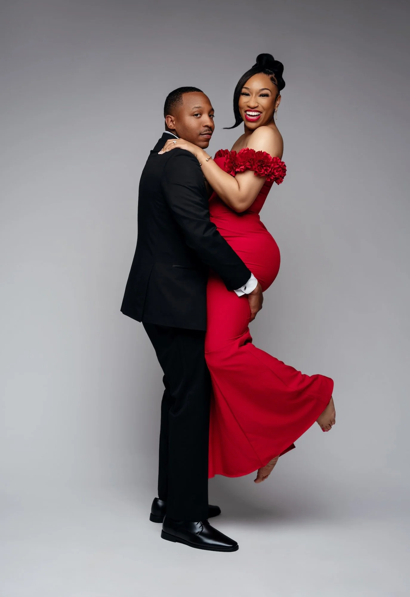 Romantic engagement photo, man lifting laughing woman in red floral dress, playful studio portrait at Filaneyka Chicago