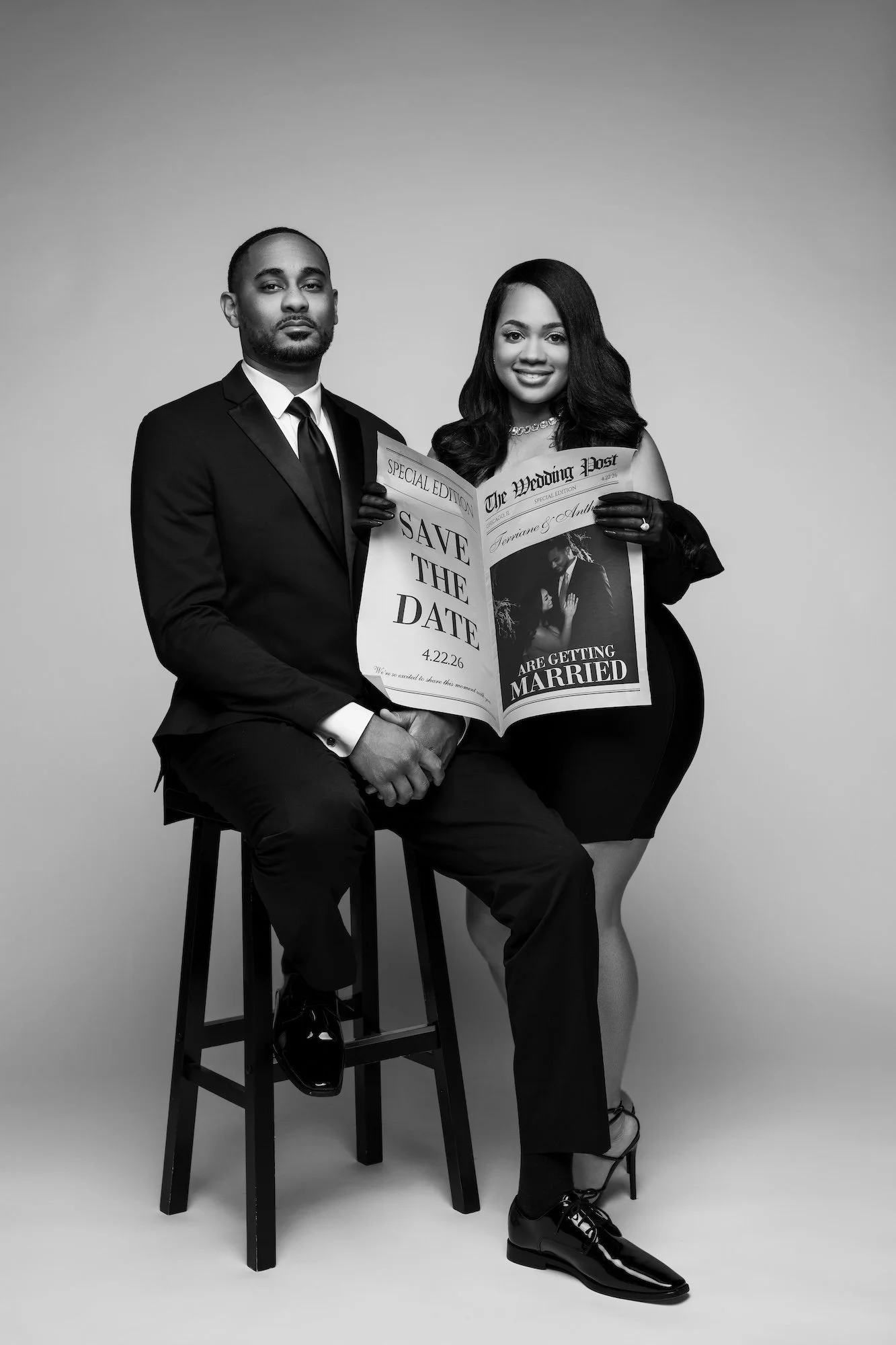 Black and white save the date engagement photo, couple on stool with newspaper prop, studio portrait at Filaneyka Chicago