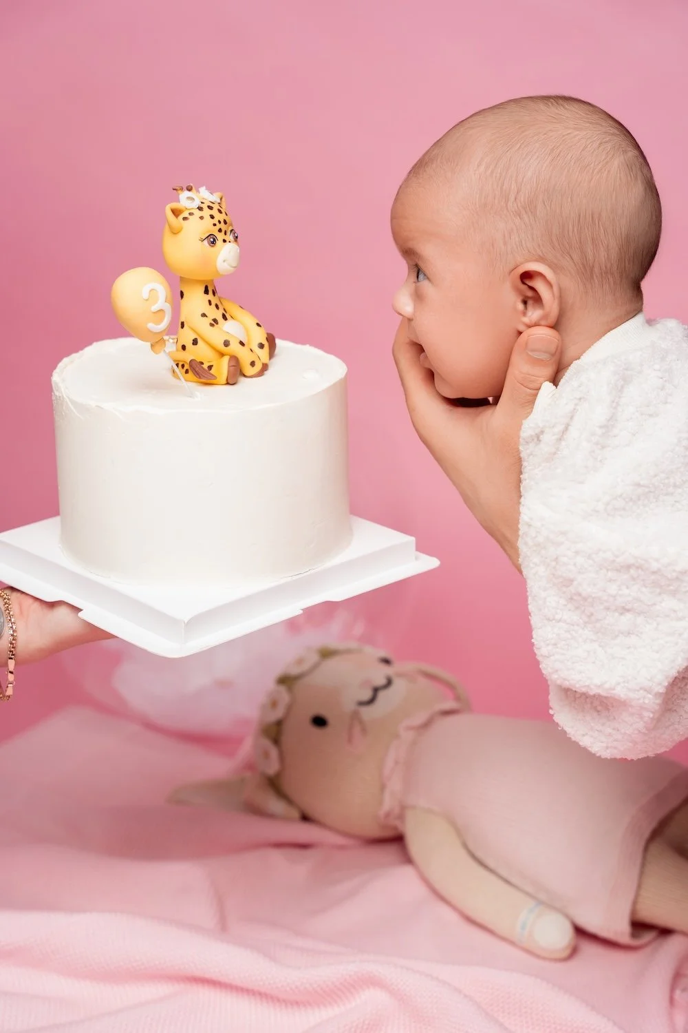  3-month baby girl in white outfit looking at her first birthday-style cake with a giraffe topper, Filaneyka Photo Studio Chicago 