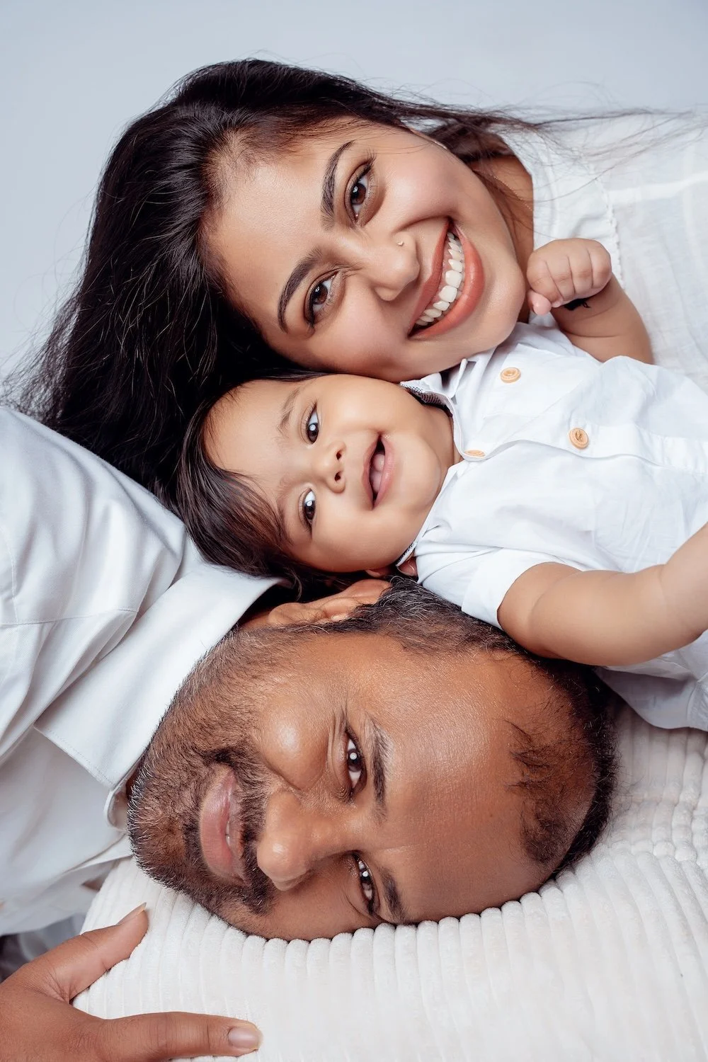  6-month baby with both parents lying on white bedding, smiling up at the camera, Filaneyka Photo Studio Chicago 
