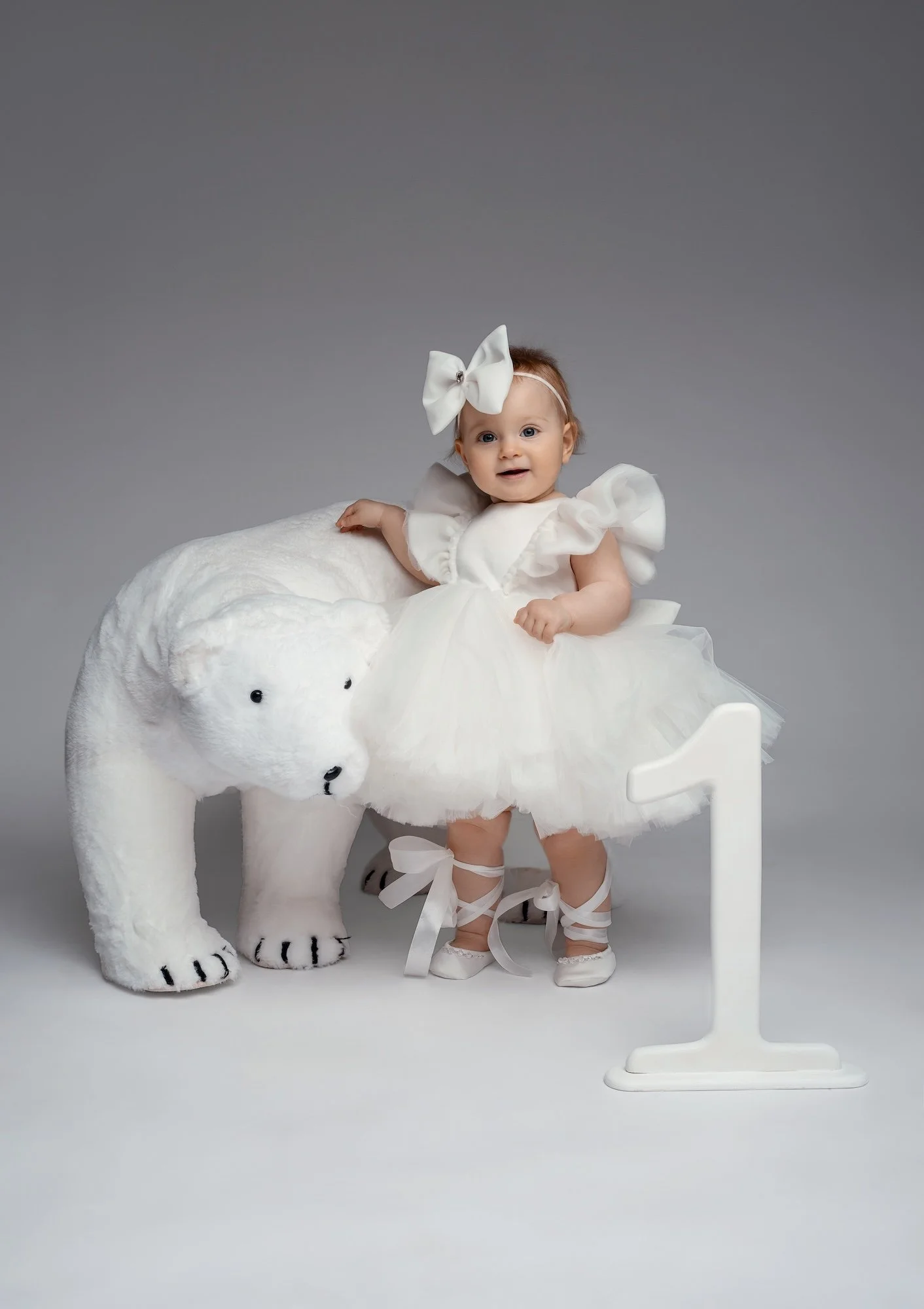  Baby girl in white tulle dress sitting on plush polar bear with number one — first birthday studio portrait 