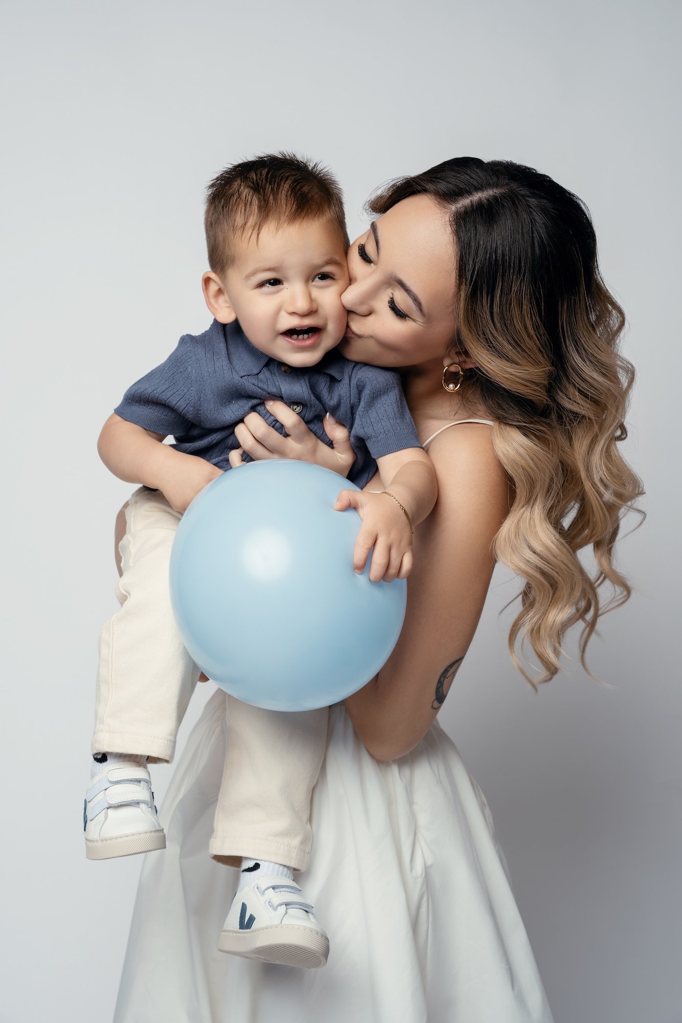  Mother holding baby boy with blue balloon in bright studio — tender family portrait for first birthday session 