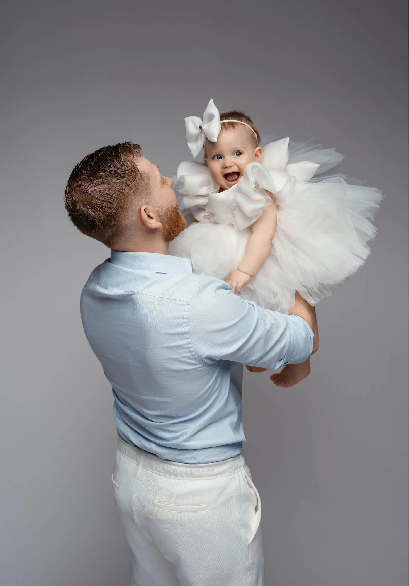  Father kissing baby girl on cheek during family studio session — heartfelt first birthday portrait 
