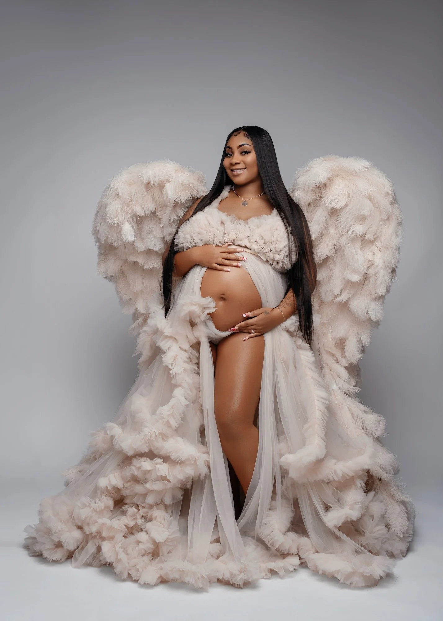  Gorgeous expectant mother in angelic cream feather wings gently holding her baby bump during luxury maternity photoshoot 