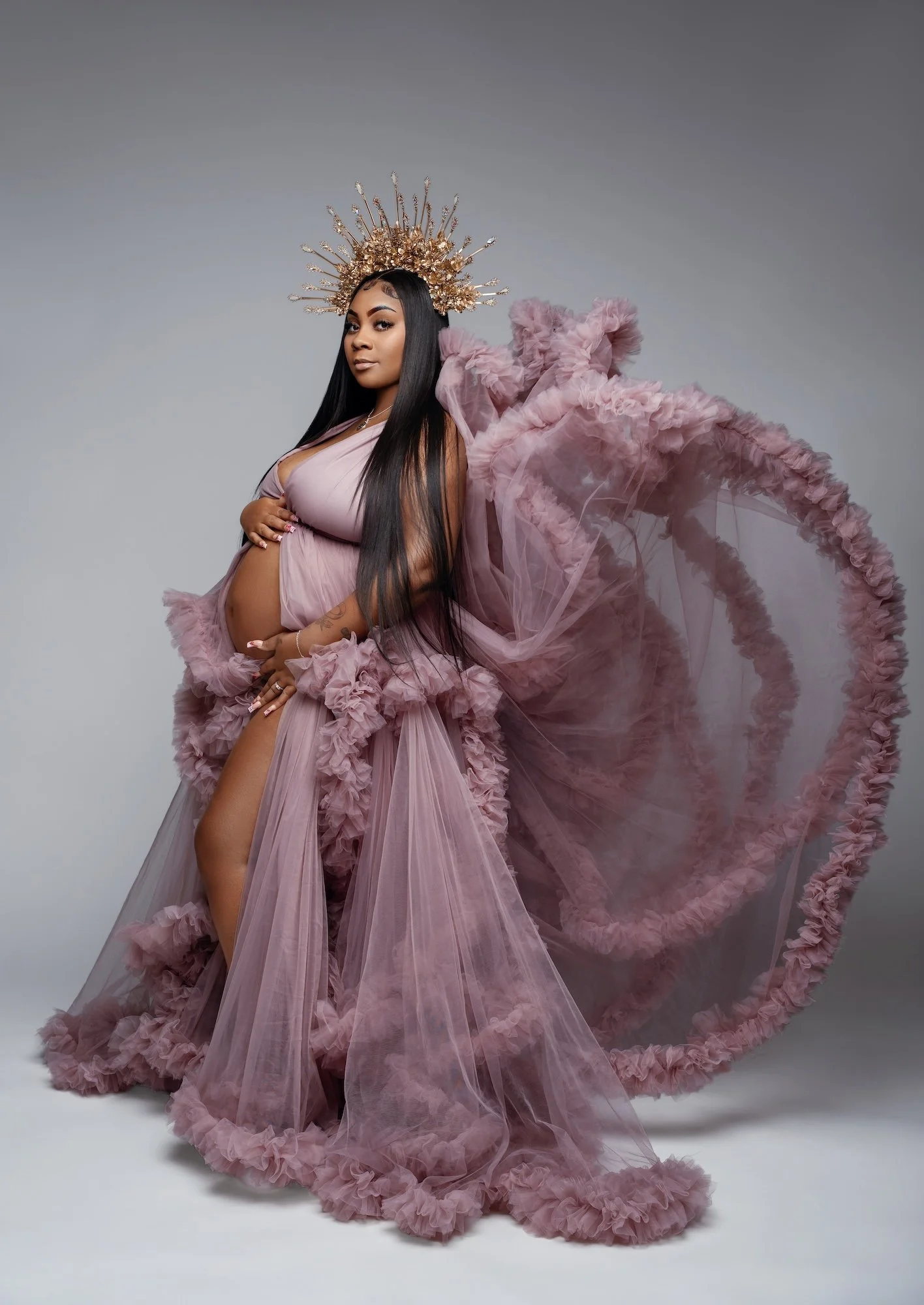  Beautiful pregnant woman in a dramatic pink ruffled maternity gown with golden crown during elegant studio maternity photoshoot 