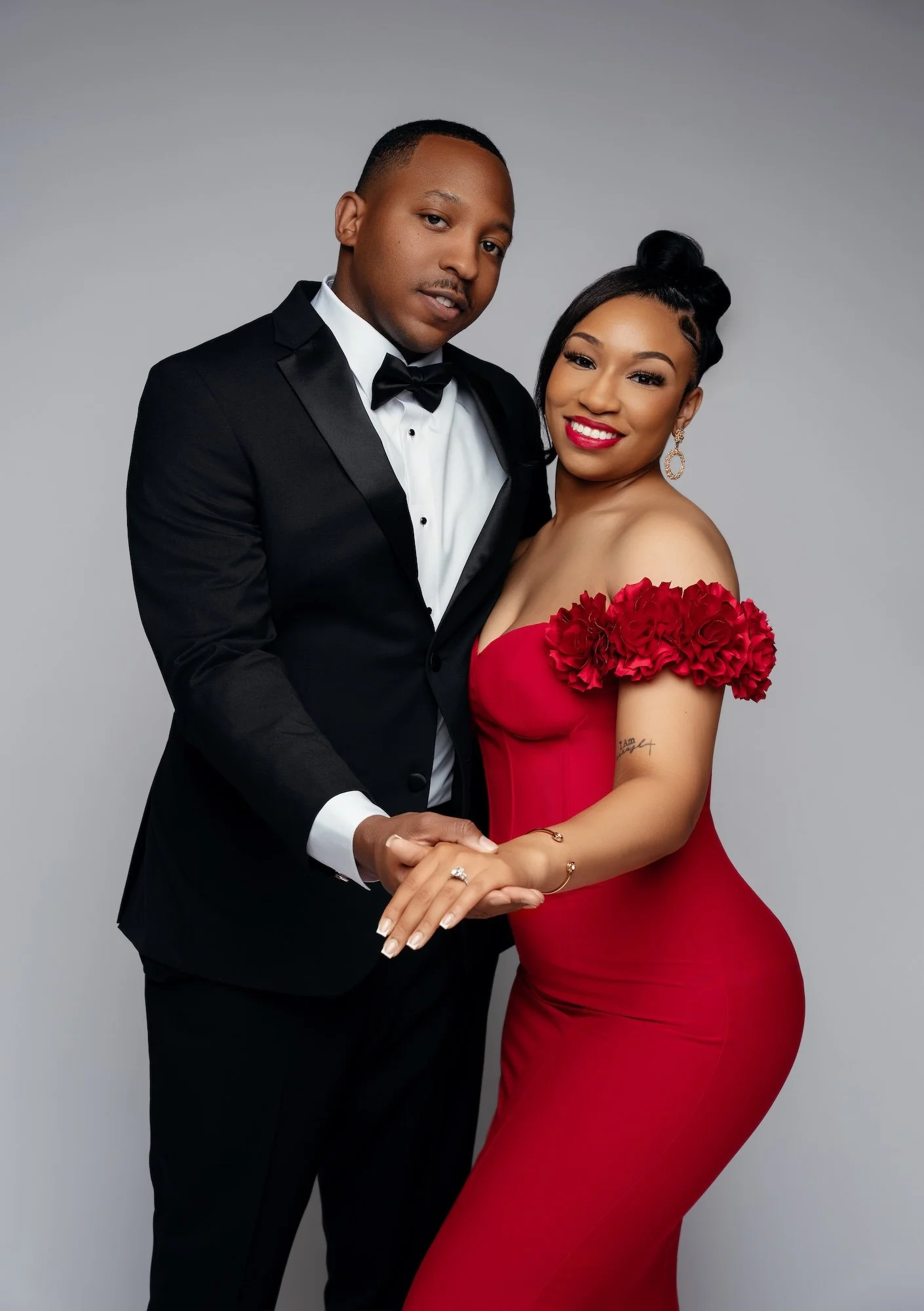 Elegant engagement couple holding hands, woman in red floral gown and man in black tuxedo, closeup studio portrait Chicago