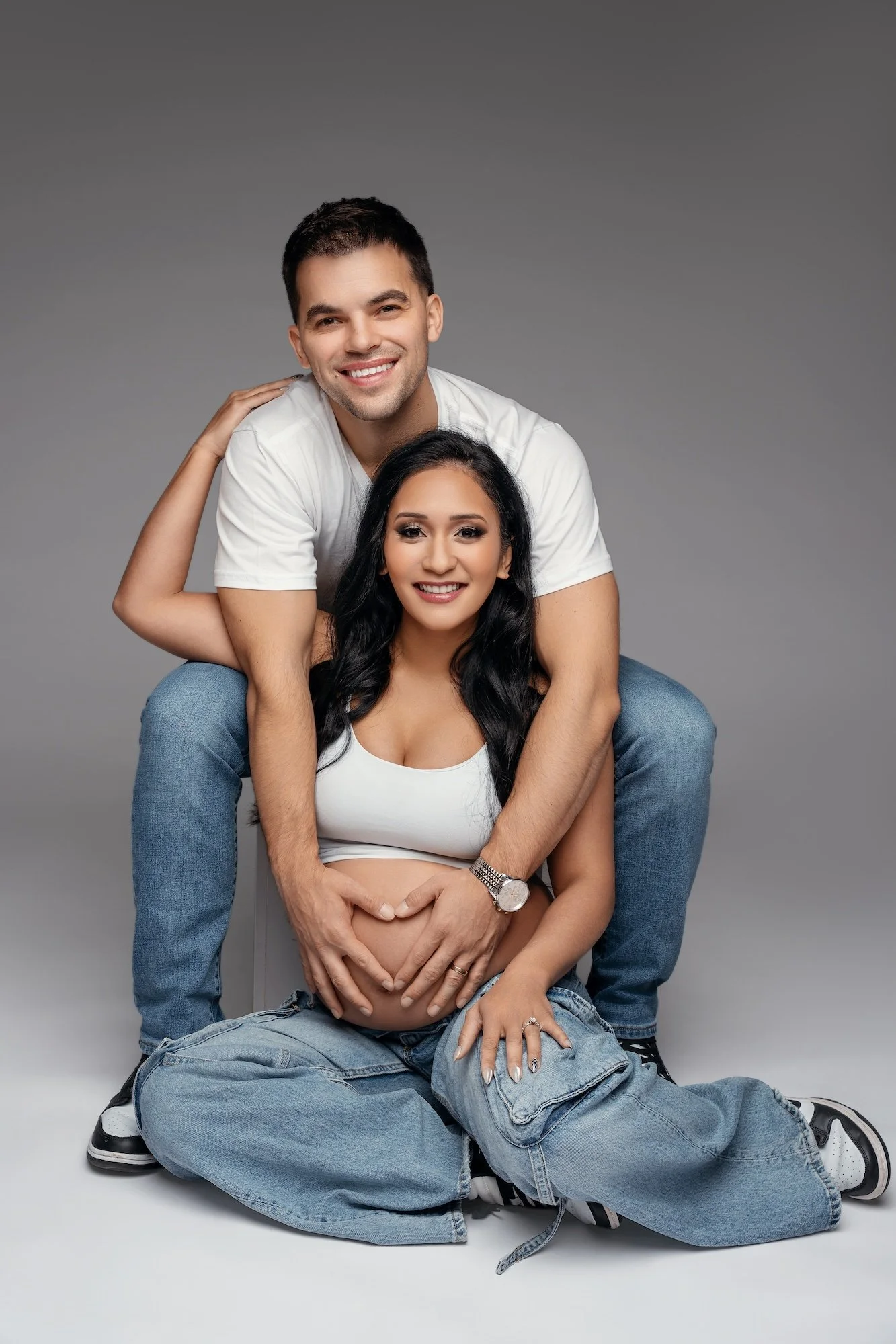  Classic couples maternity outfit idea: husband in white t-shirt and jeans making a heart with his hands on his wife's baby bump, Chicago studio 