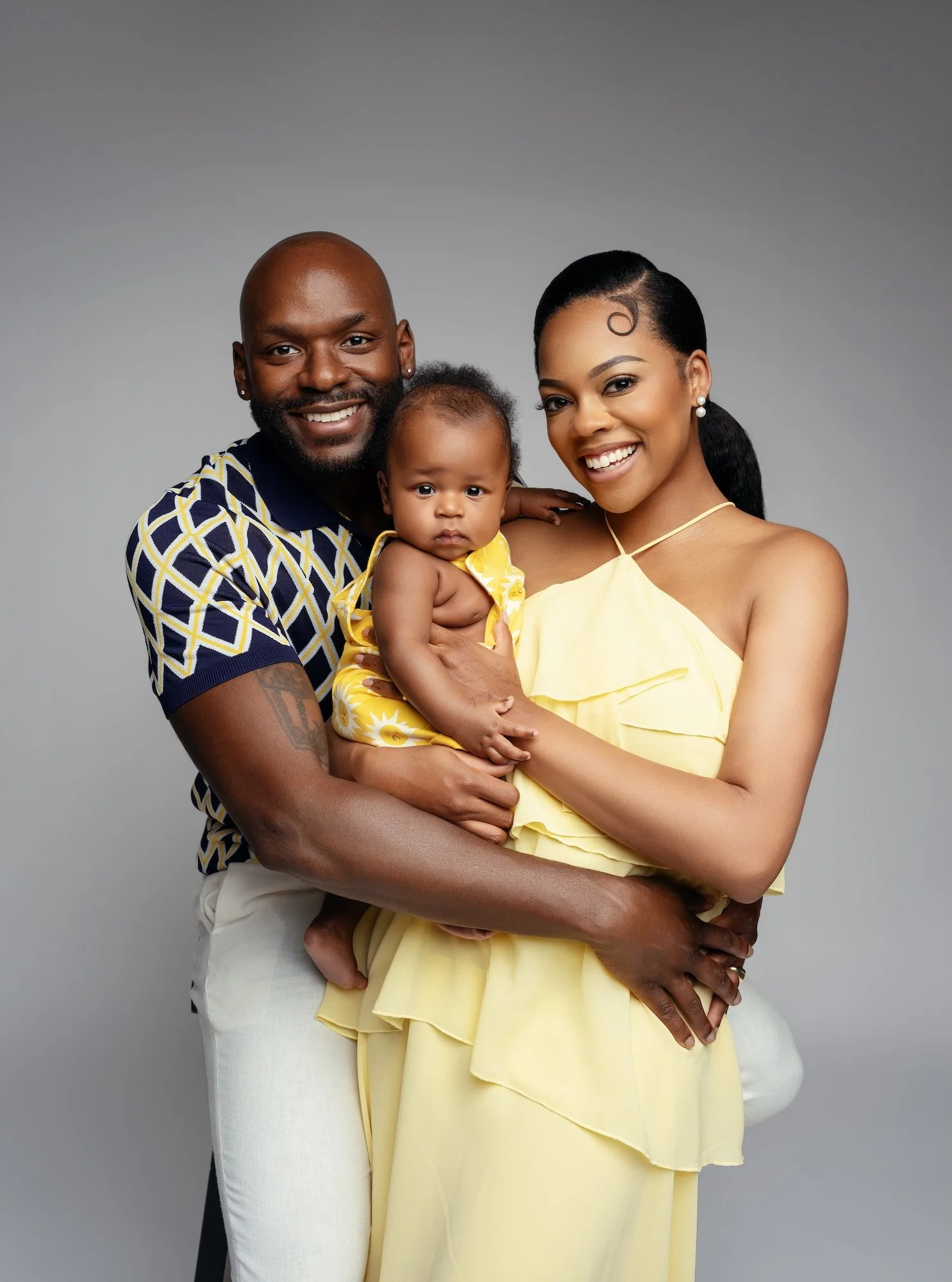  Smiling family in coordinated yellow and navy outfits holding their baby during a studio family photo session in Chicago 