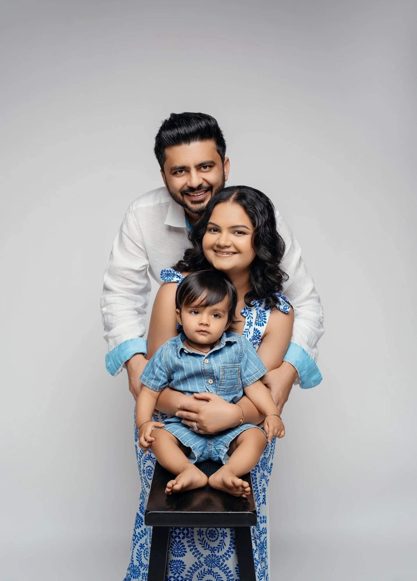  Family portrait with baby sitting on a stool, parents in white and blue coordinated outfits, studio family photography in Chicago 