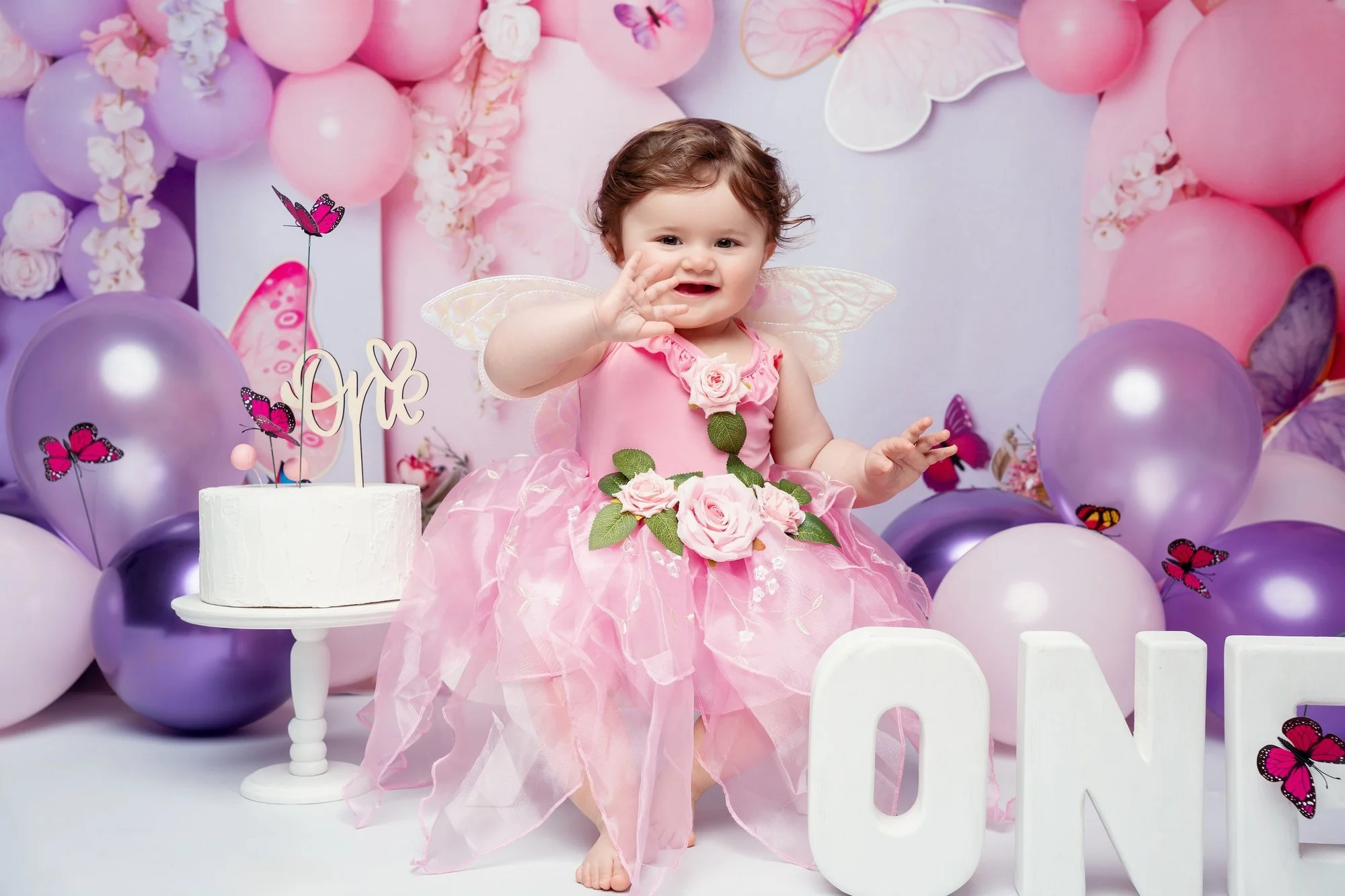 One-year-old girl laughing in a pink tulle dress among balloons and ONE letters during a first birthday photo session at a downtown Chicago studio
