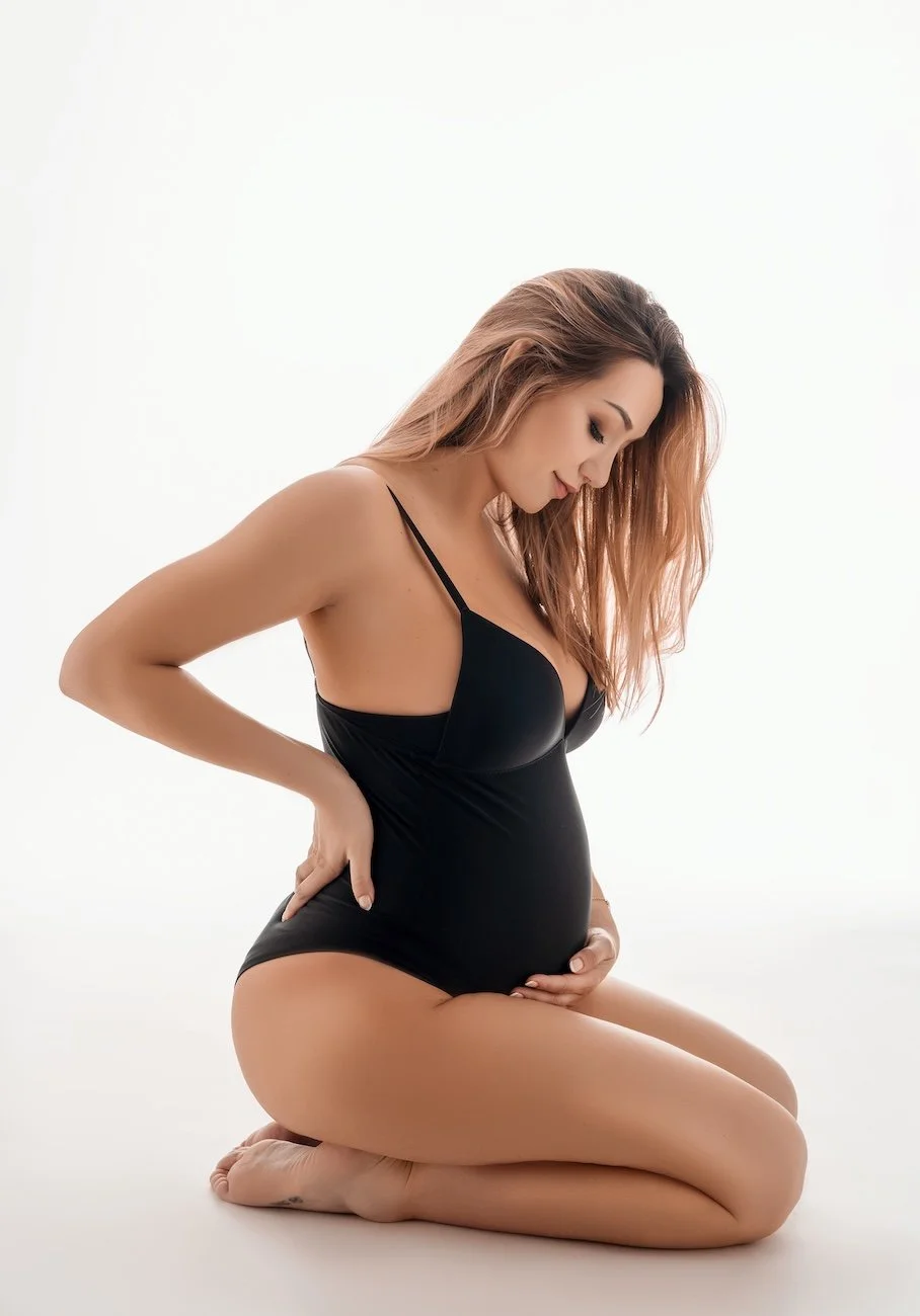 Pregnant woman in black one-piece, holding baby bump, studio portrait