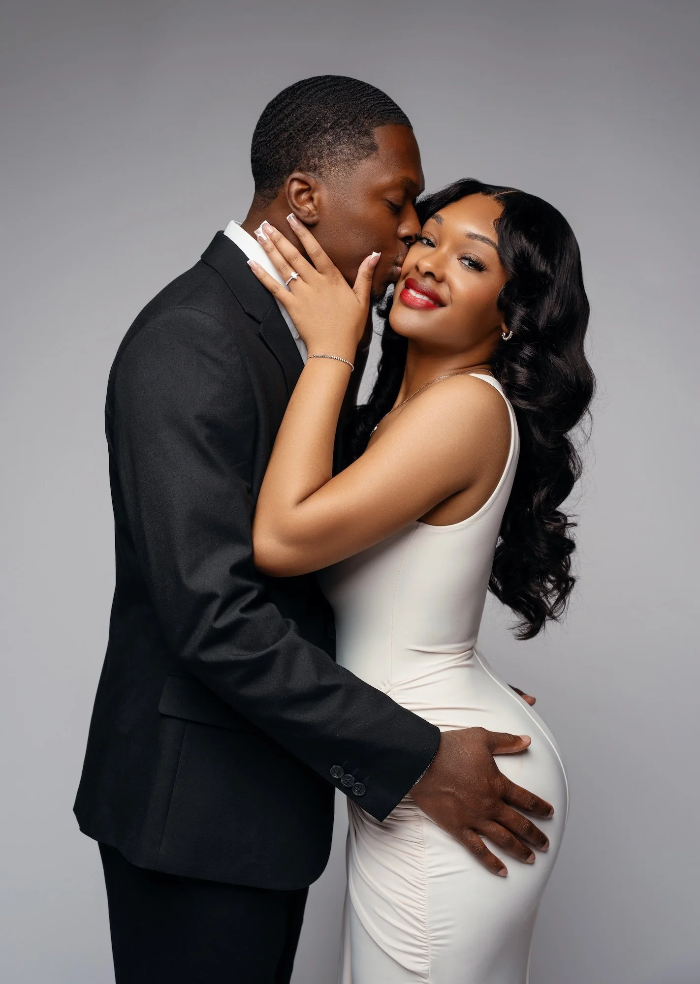 Romantic engagement portrait, man kissing woman's cheek from behind with gentle embrace, gray studio backdrop, Chicago engagement photography