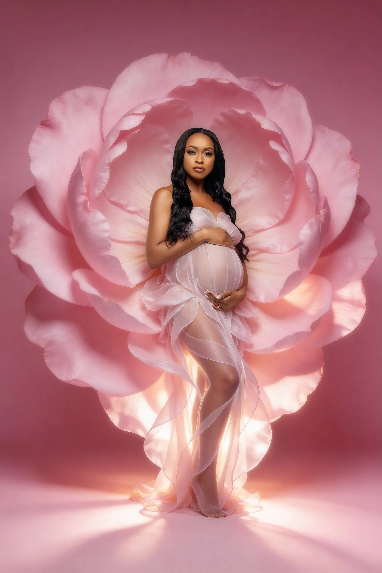 Luxury fine-art maternity portrait: pregnant woman in a sheer white dress framed by a giant pink peony bloom
