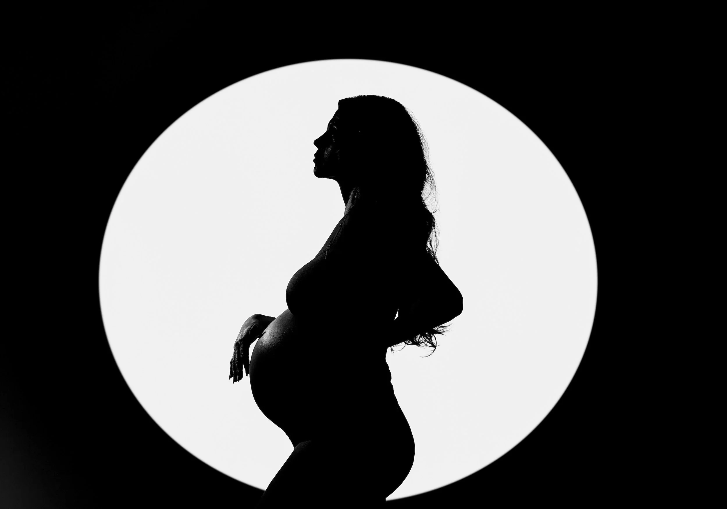 Fine-art maternity portrait: dramatic silhouette of a pregnant woman in a spotlight