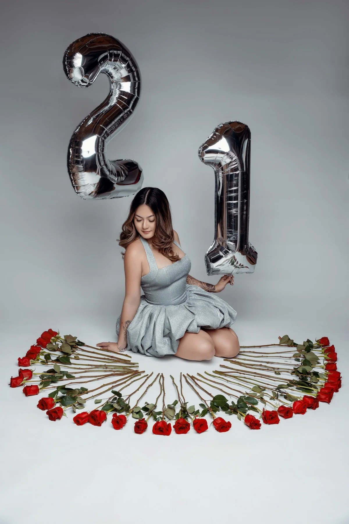 21st birthday photoshoot of a young woman in a sparkling dress posing with "21" balloons and red roses