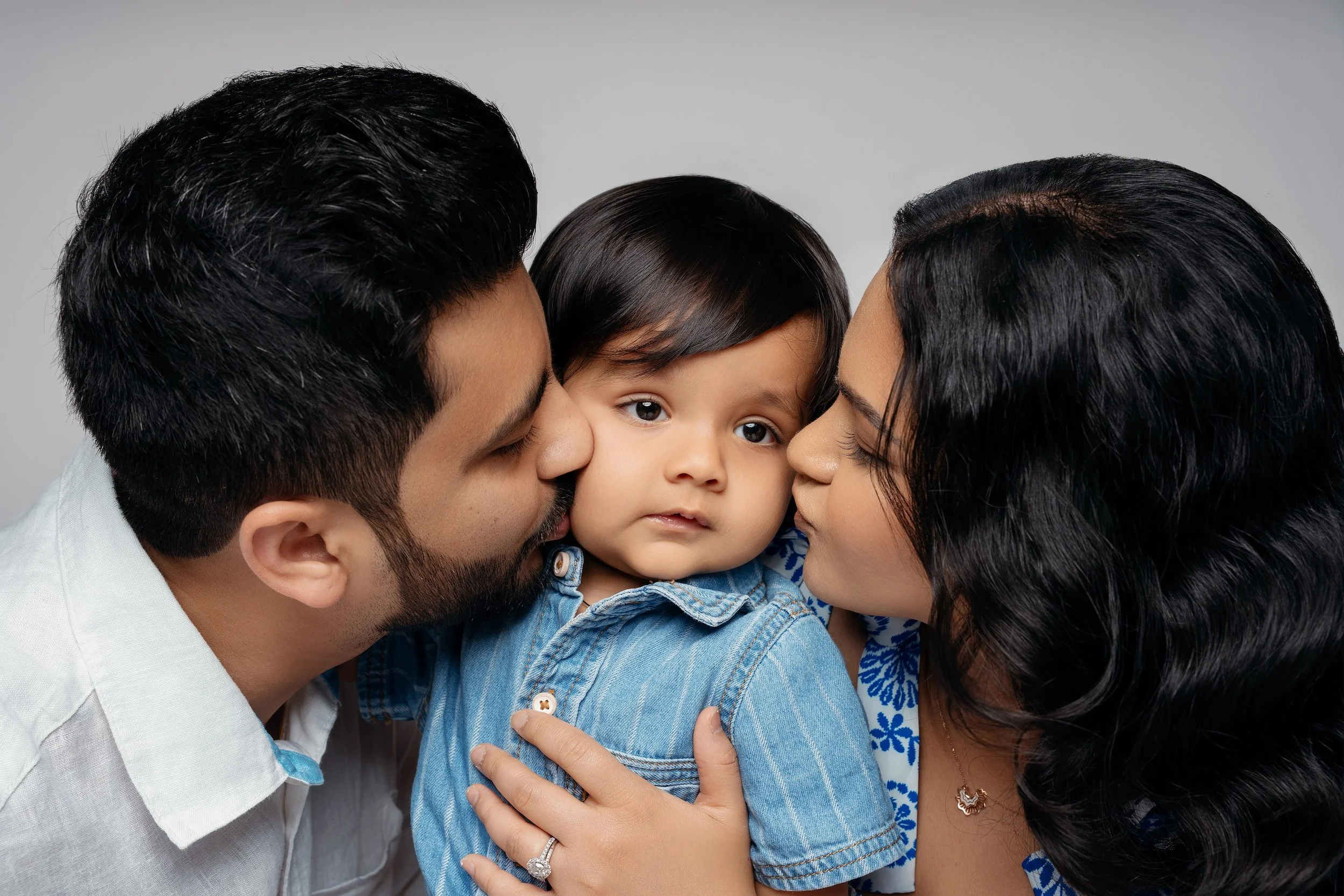 Parents kissing their baby on the cheeks during a fall studio family photoshoot in Chicago, wearing coordinated denim and white outfits