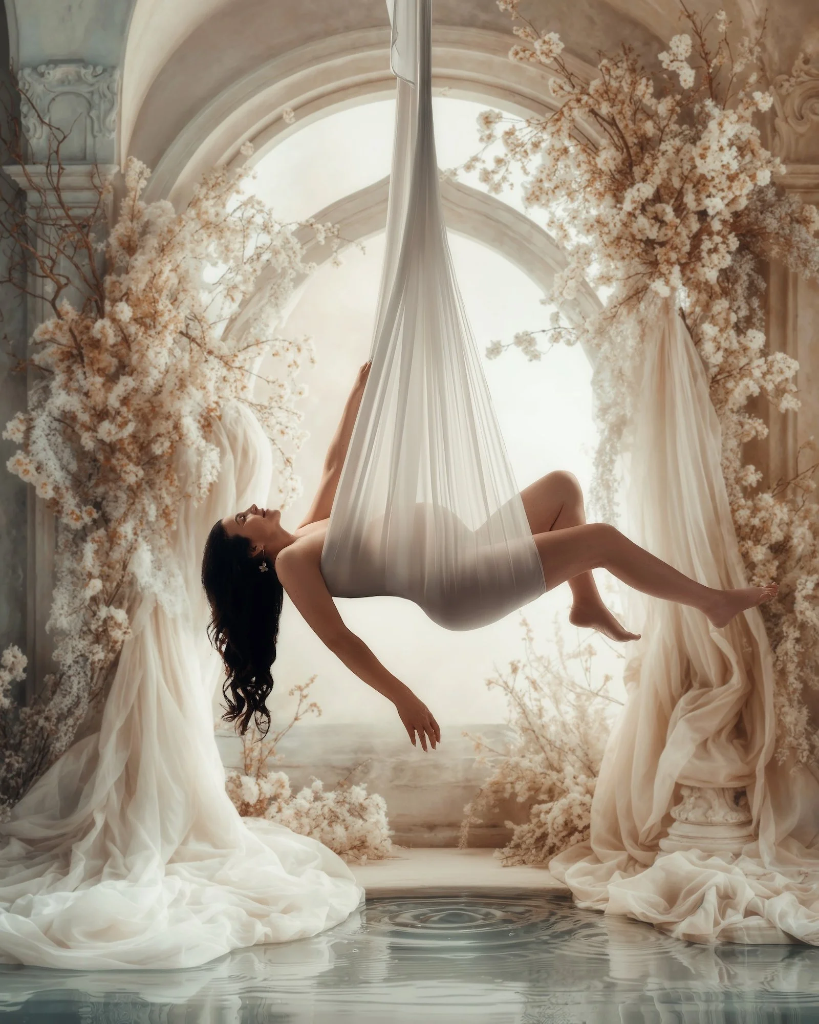 Exclusive fine-art maternity portrait: pregnant woman in a flowing white gown reclining in a flower-filled boat on dreamy turquoise water, surrounded by lush blooms