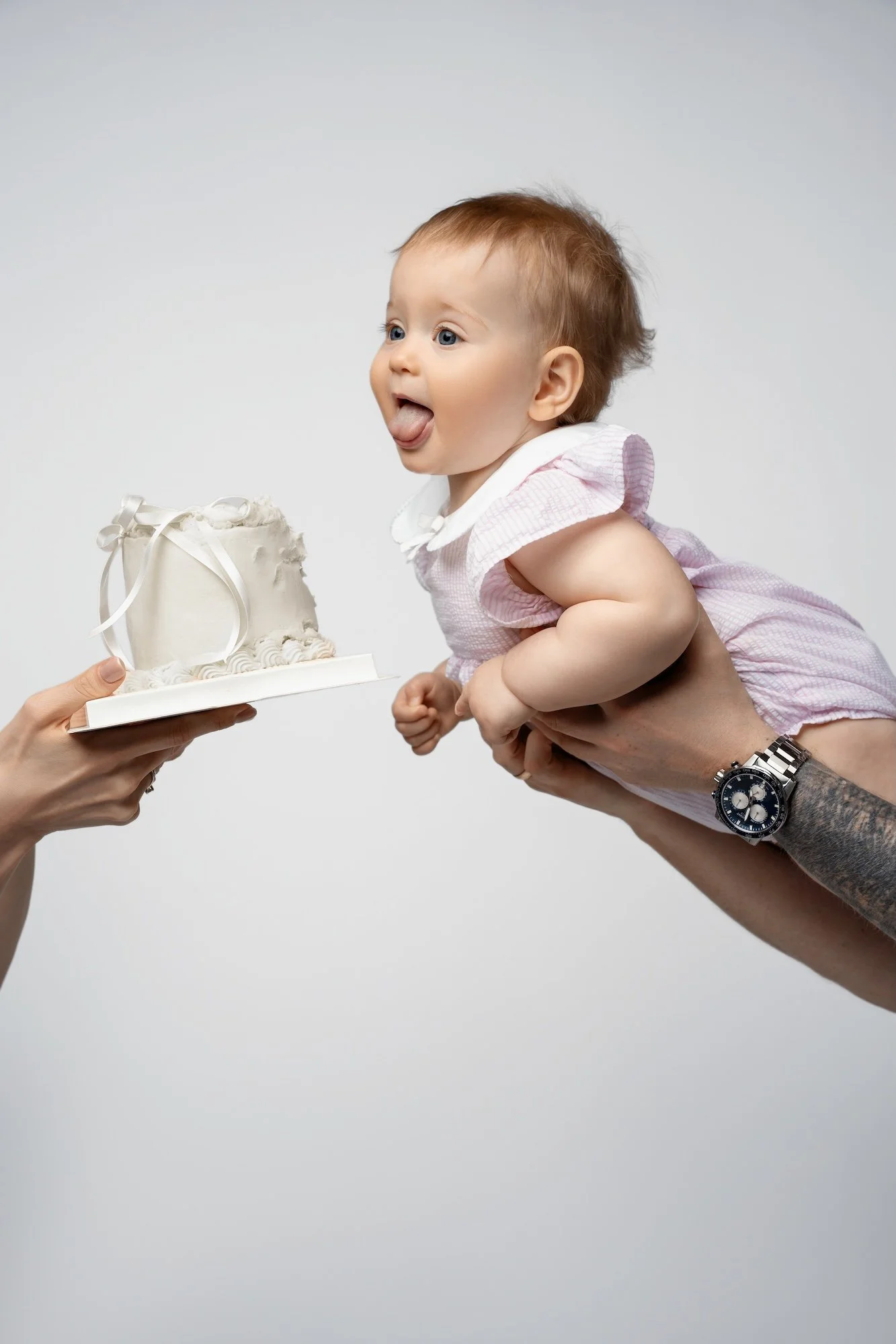 Boutique cake smash session: baby reaching toward a small white cake for a first birthday