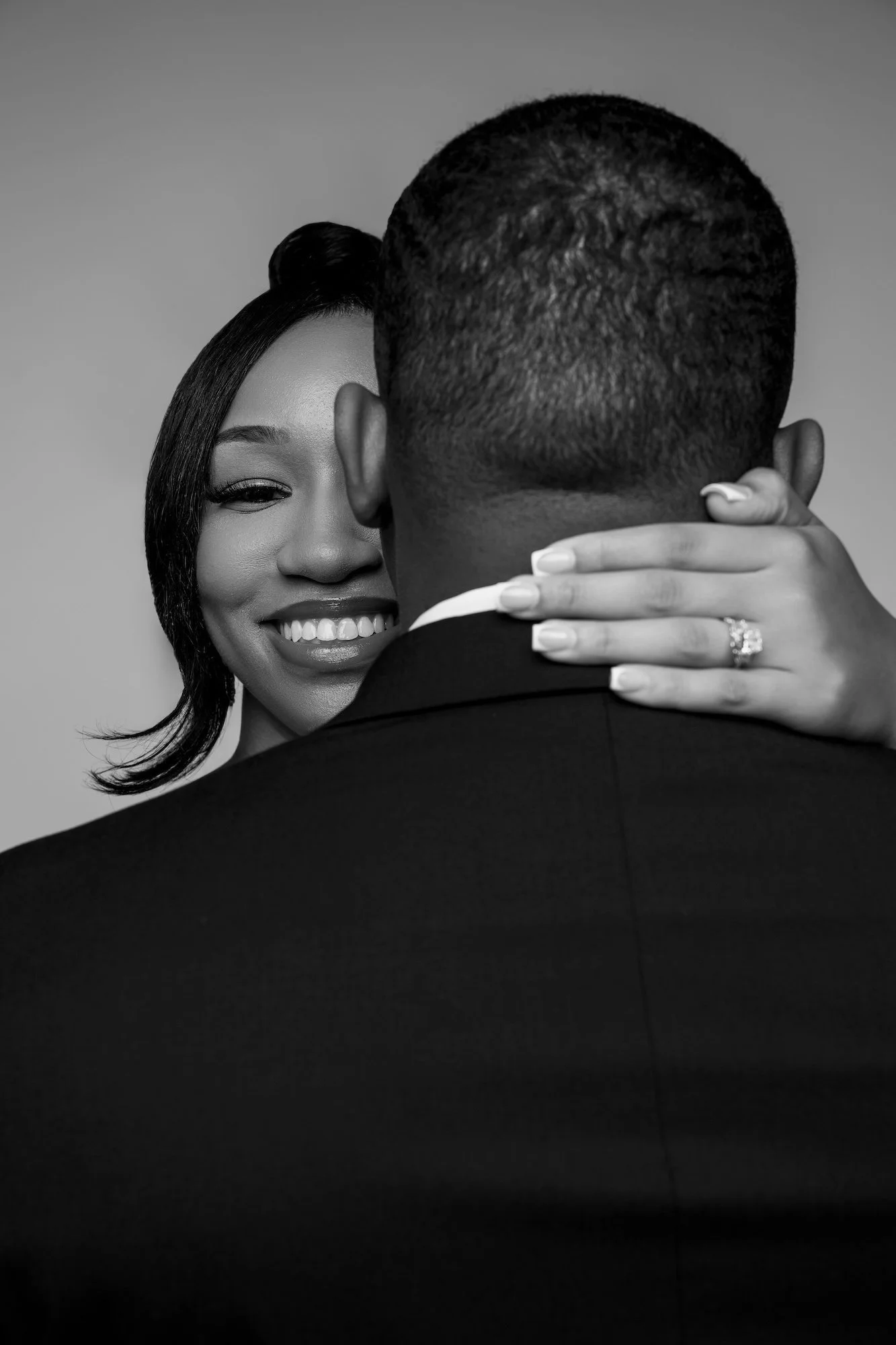 Black and white engagement ring reveal, woman smiling over man's shoulder with diamond ring, studio photography at Filaneyka Chicago
