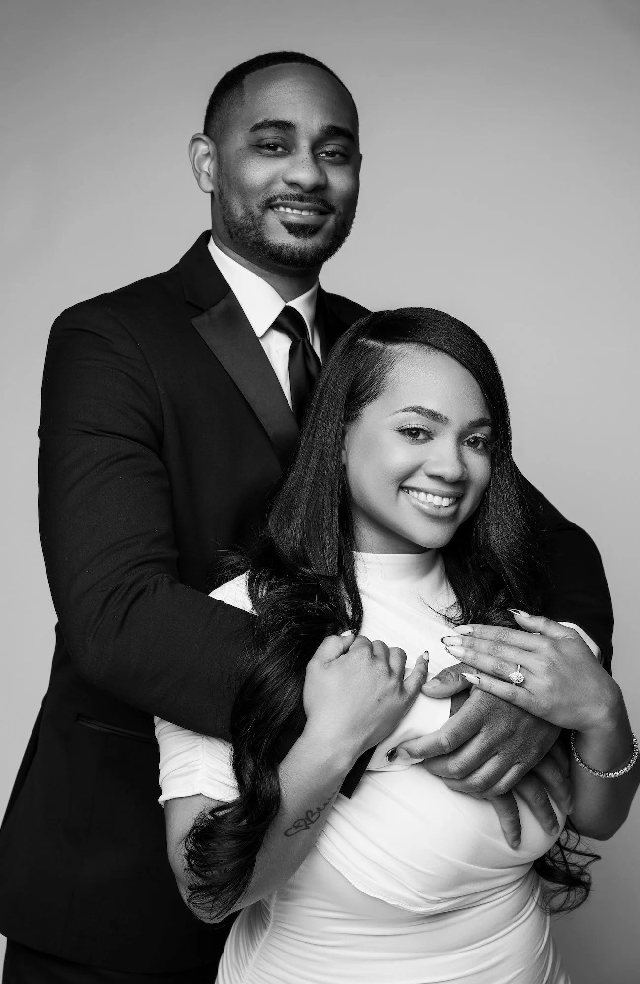 Black and white warm engagement hug, man embracing woman in white turtleneck from behind, joyful studio portrait at Filaneyka Chicago