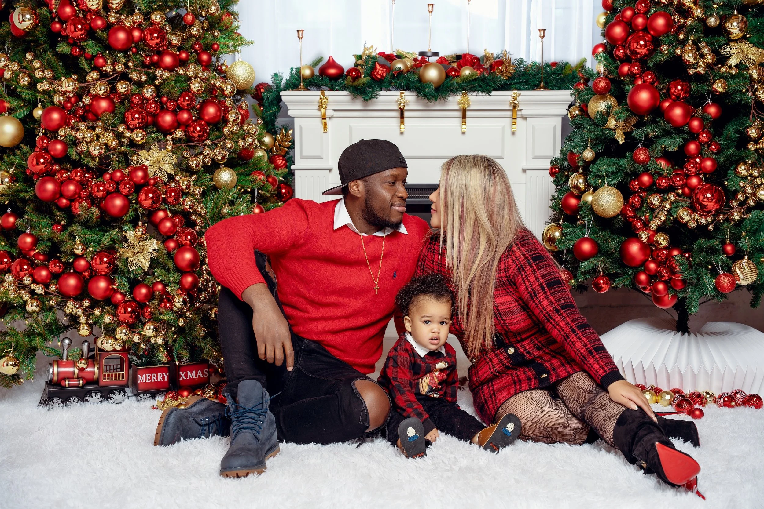 Christmas family photo session in Chicago studio: family in matching red and plaid holiday outfits by the fireplace and Christmas tree.