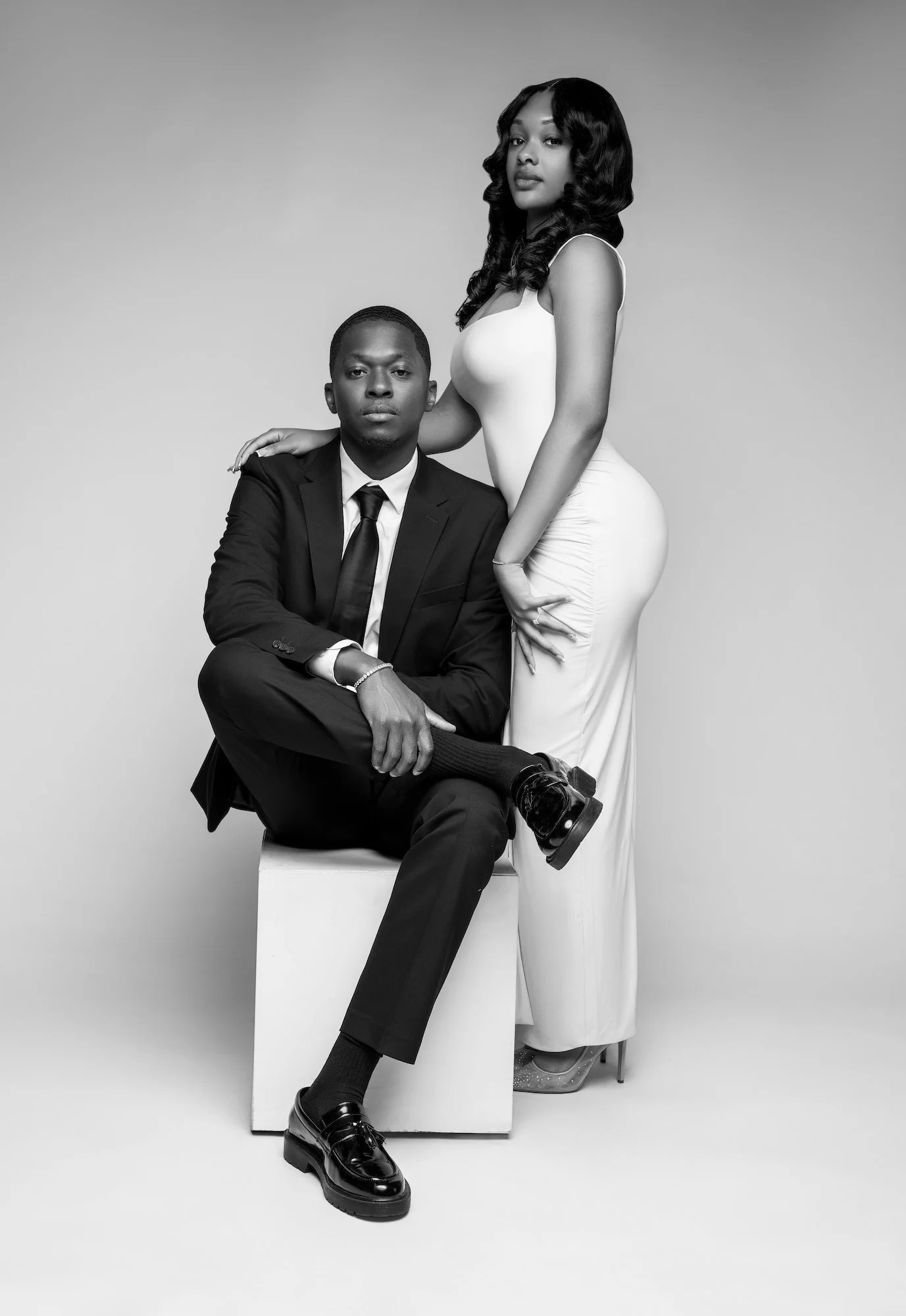 Black and white elegant engagement portrait, man seated with woman standing behind, formal studio photography at Filaneyka Chicago
