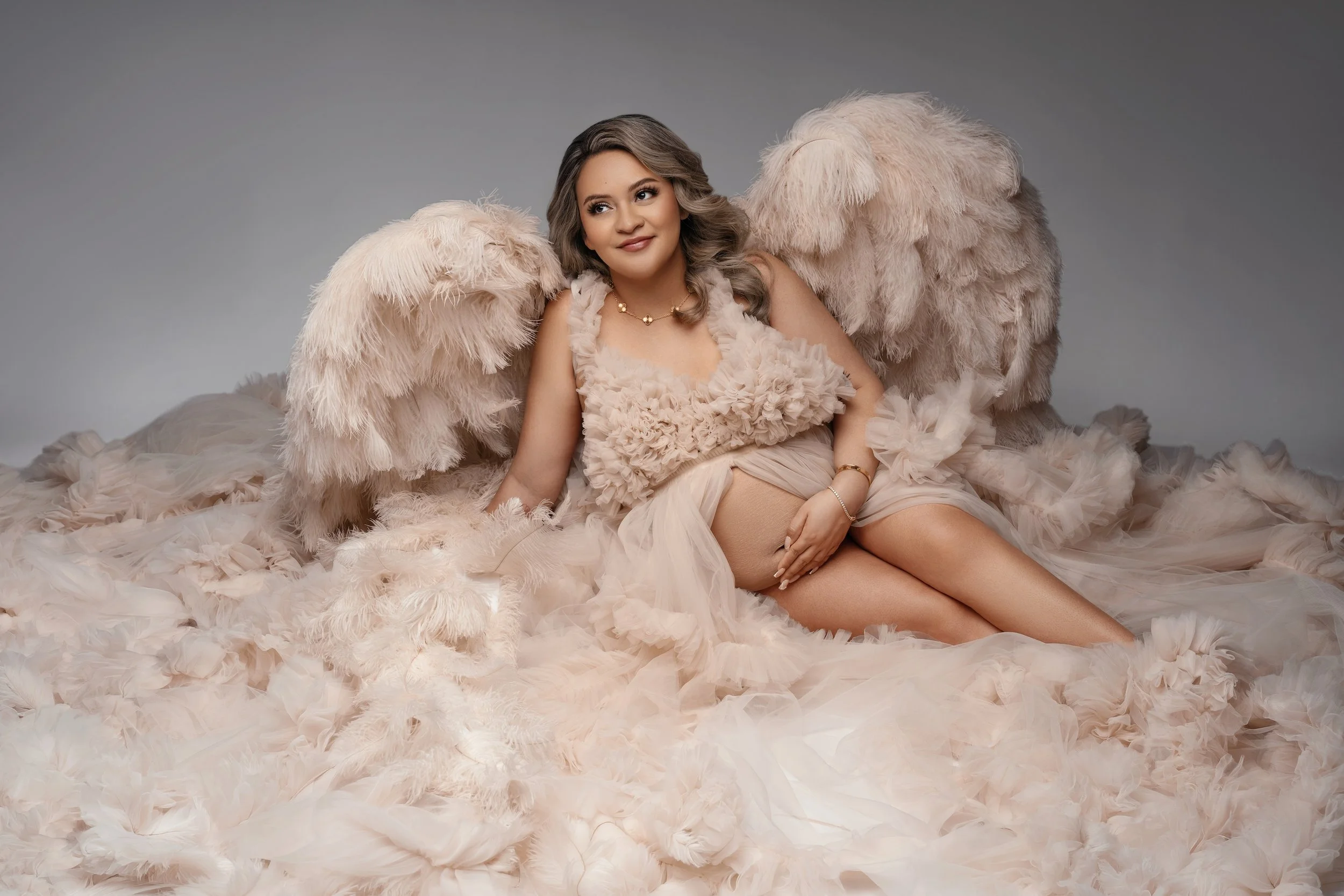 Luxury maternity studio portrait: pregnant woman in a feathered gown with angel wings